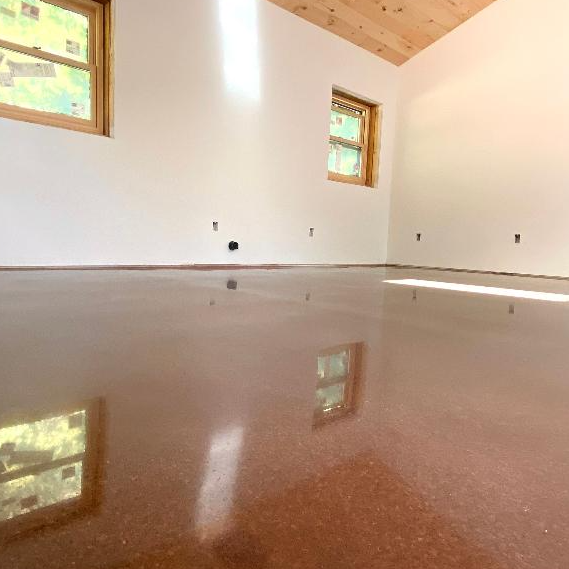 Empty room with polished wooden floor, white walls, two small windows, and a sloped wooden ceiling.