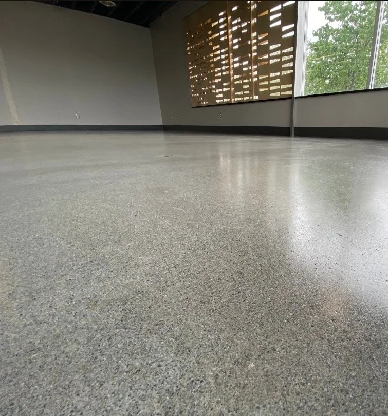Empty room with a polished concrete floor, a wooden slat wall, and a large window showing trees outside.