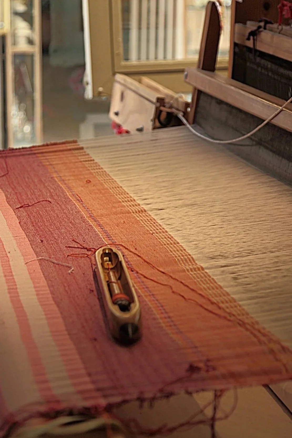 Close-up of a sewing machine with a partially sewn red and pink striped fabric, showing the machine's needle and some attached threads.