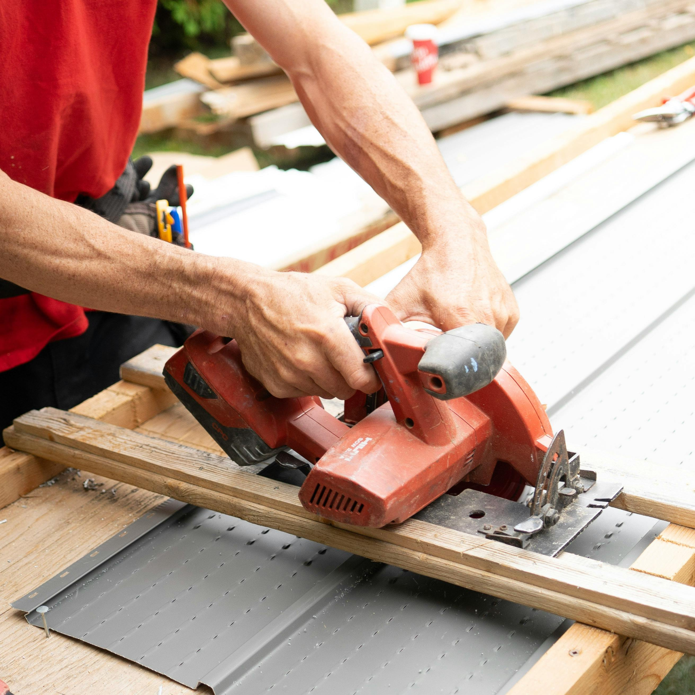Person using a power saw to cut a piece of gray metal on a woodworking project outdoors.