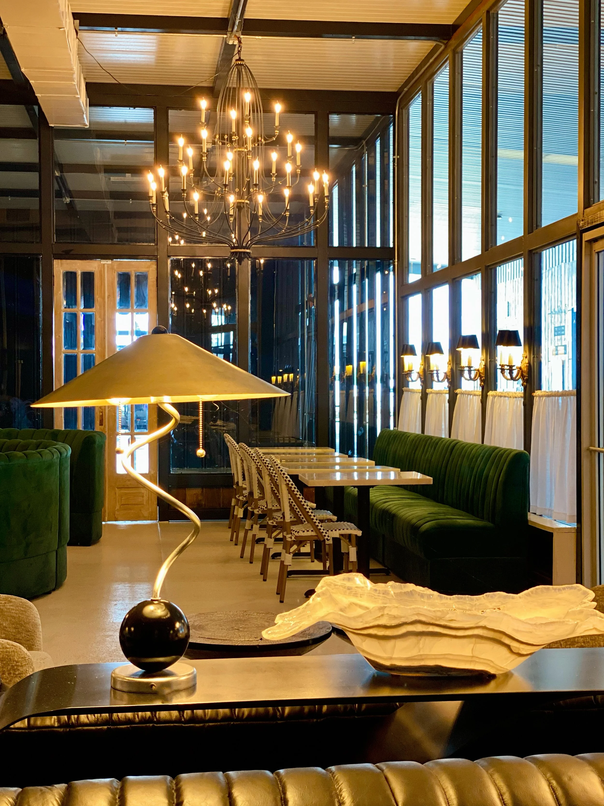 Dining room interior at DUO Modern with a brass chandelier, velvet green booths, and floor-to-ceiling windows