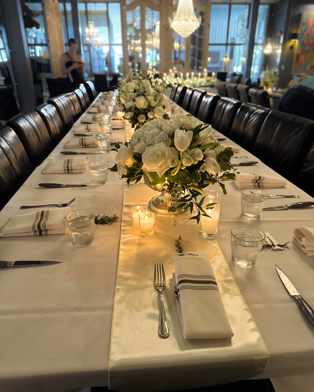 Elegant banquet table set for a formal event with white floral centerpieces, candles, and tableware in a decorated dining area.