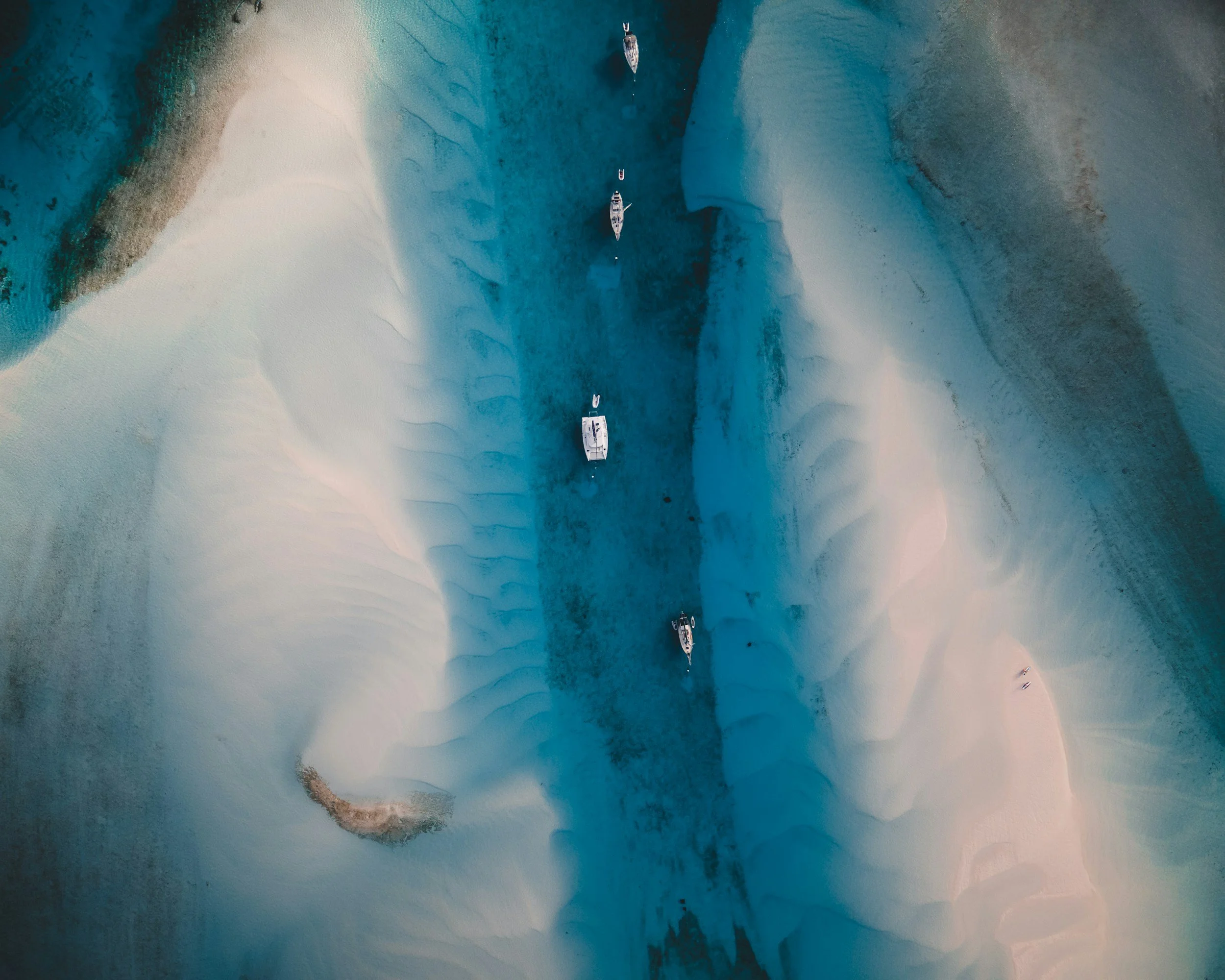 Aerial view of clear turquoise waters with a narrow channel and small boats anchored nearby.