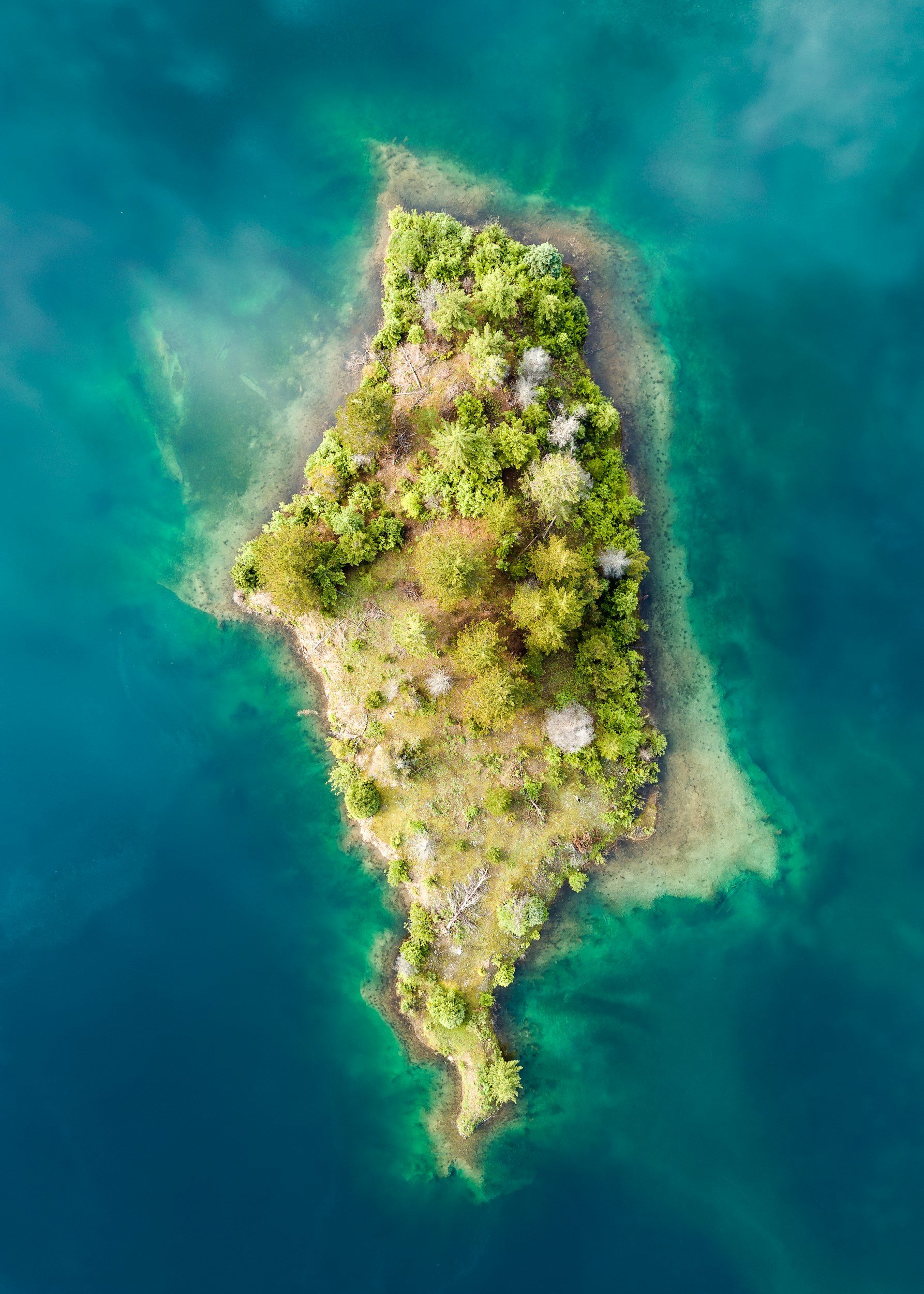 Aerial view of a small, forested island surrounded by turquoise water.