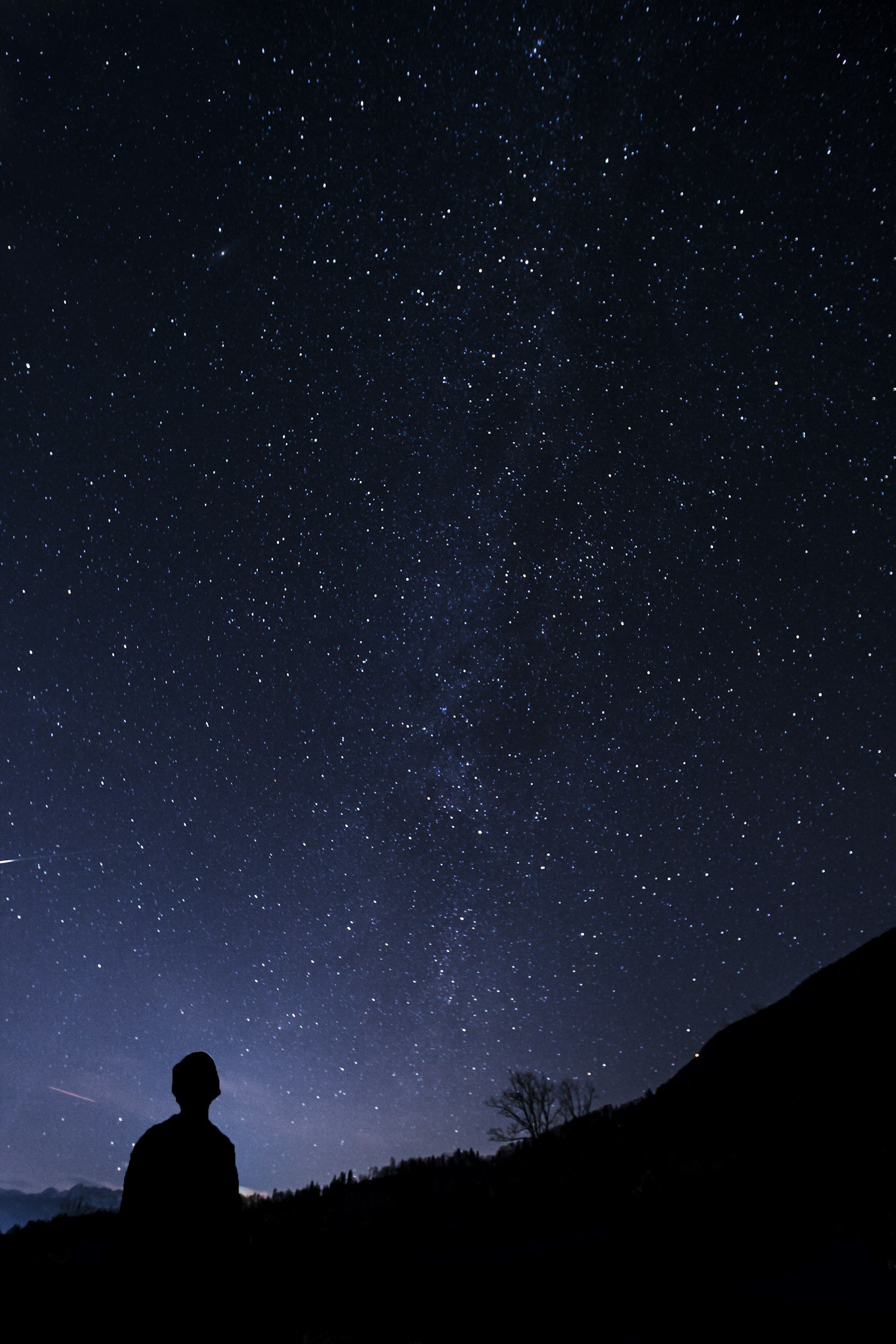 Silhouette of a person sitting on a hill overlooking a starry night sky.
