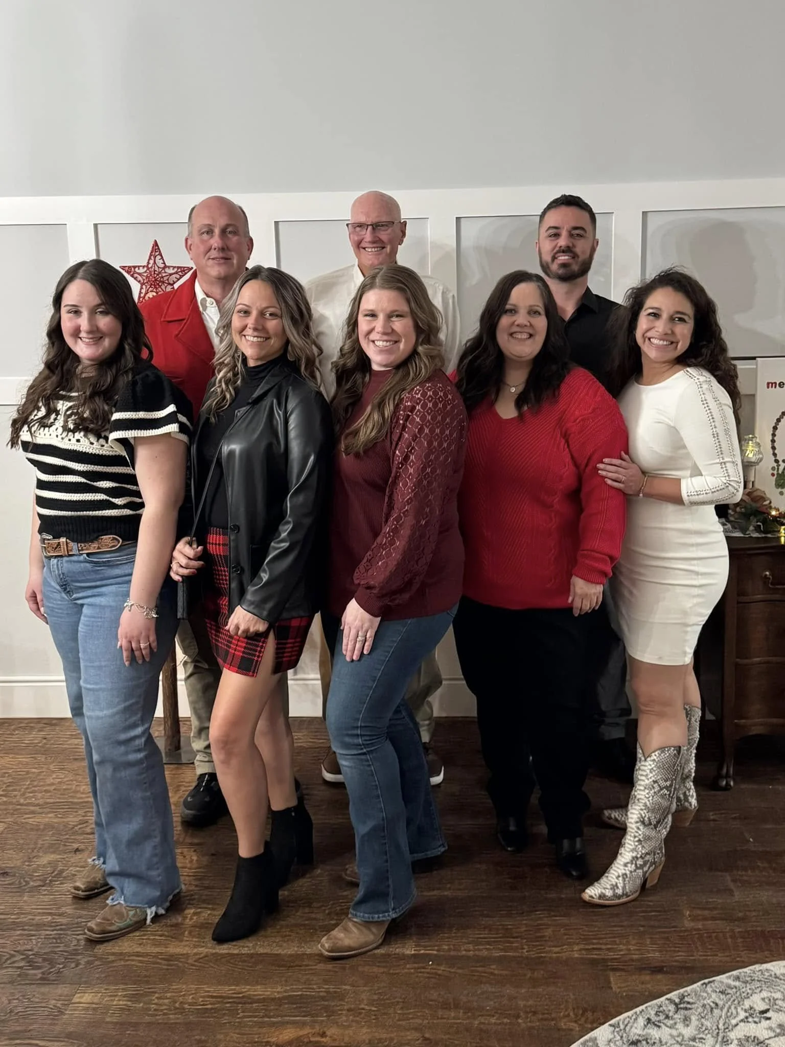 Group of eight people standing together indoors, smiling for a photo, with Christmas decorations in the background.