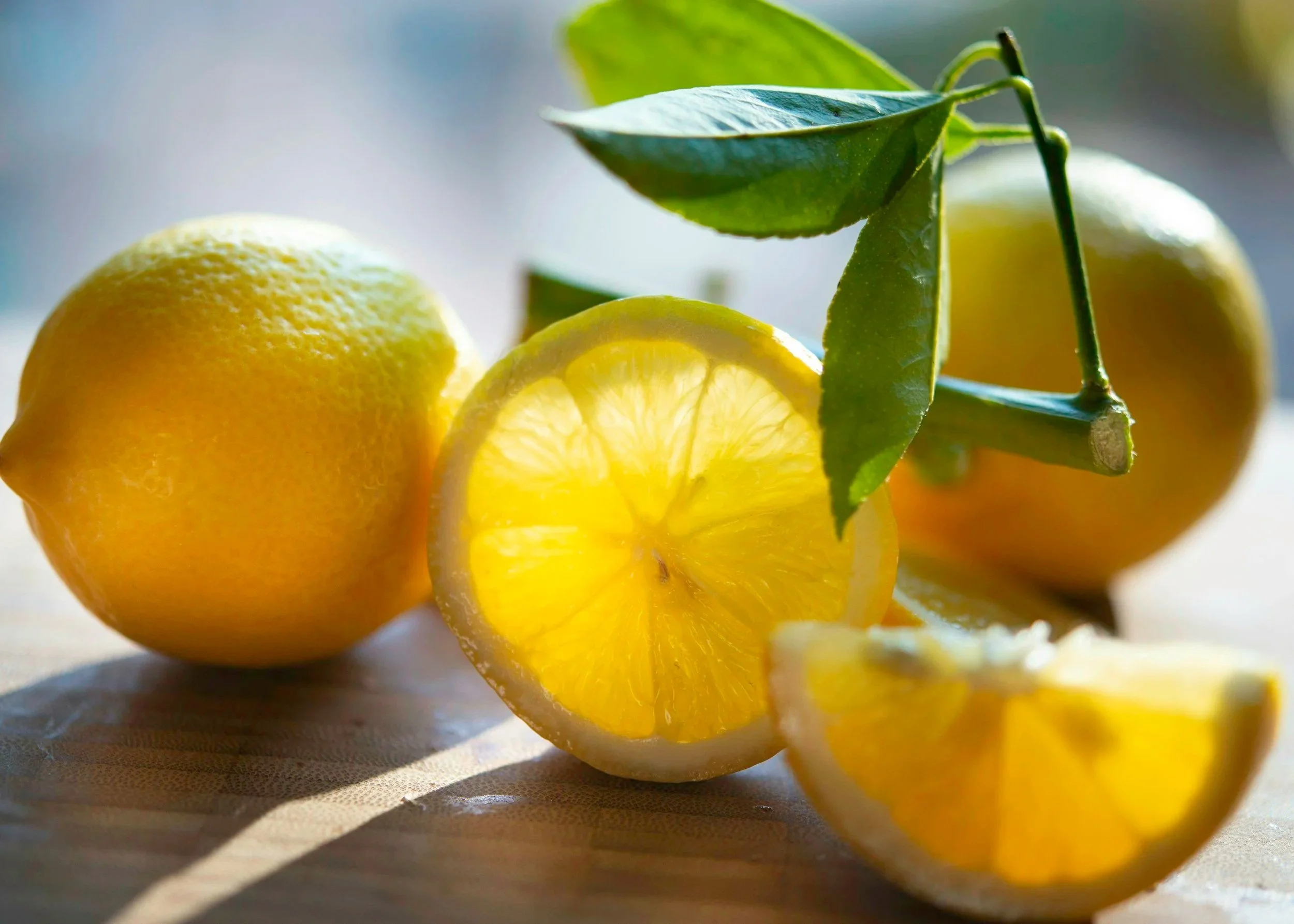Fresh yellow lemons, some whole and some sliced open, with green leaves on a wooden surface.