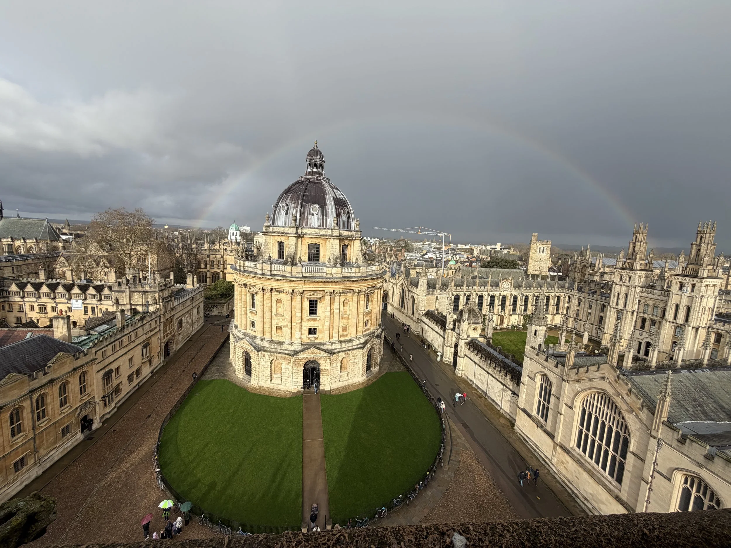Aerial view of Oxford University buildings, with a rainbow in the cloudy sky above.