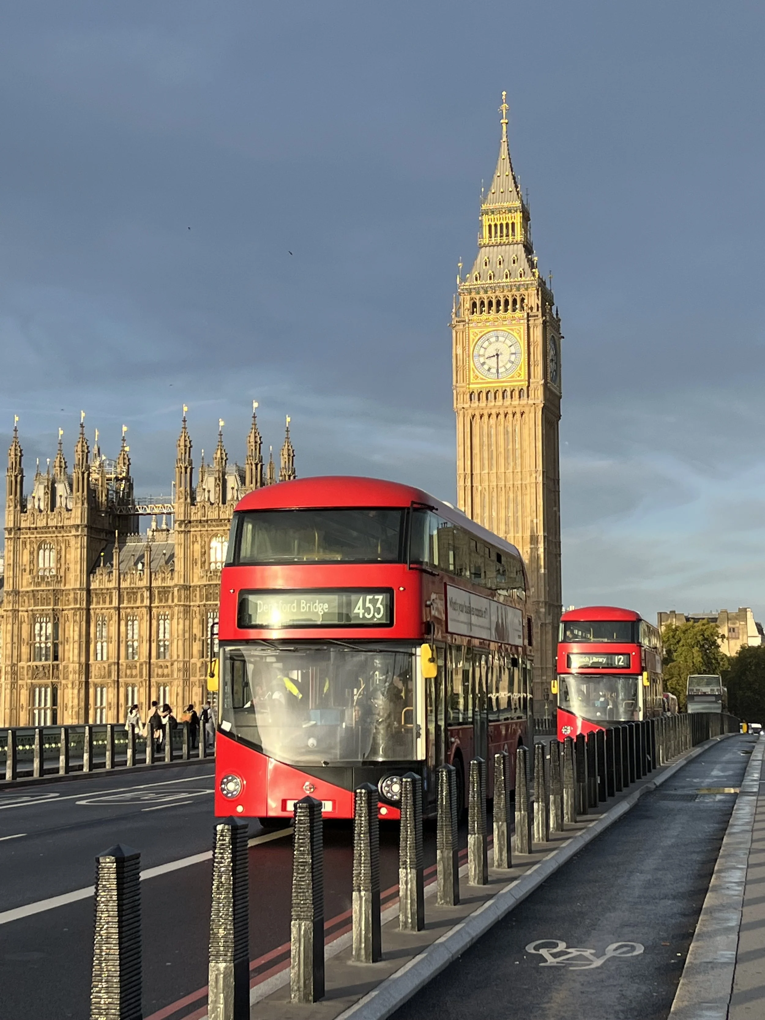 Red double-decker buses on a bridge in London with Big Ben clock tower in the background during daylight.
