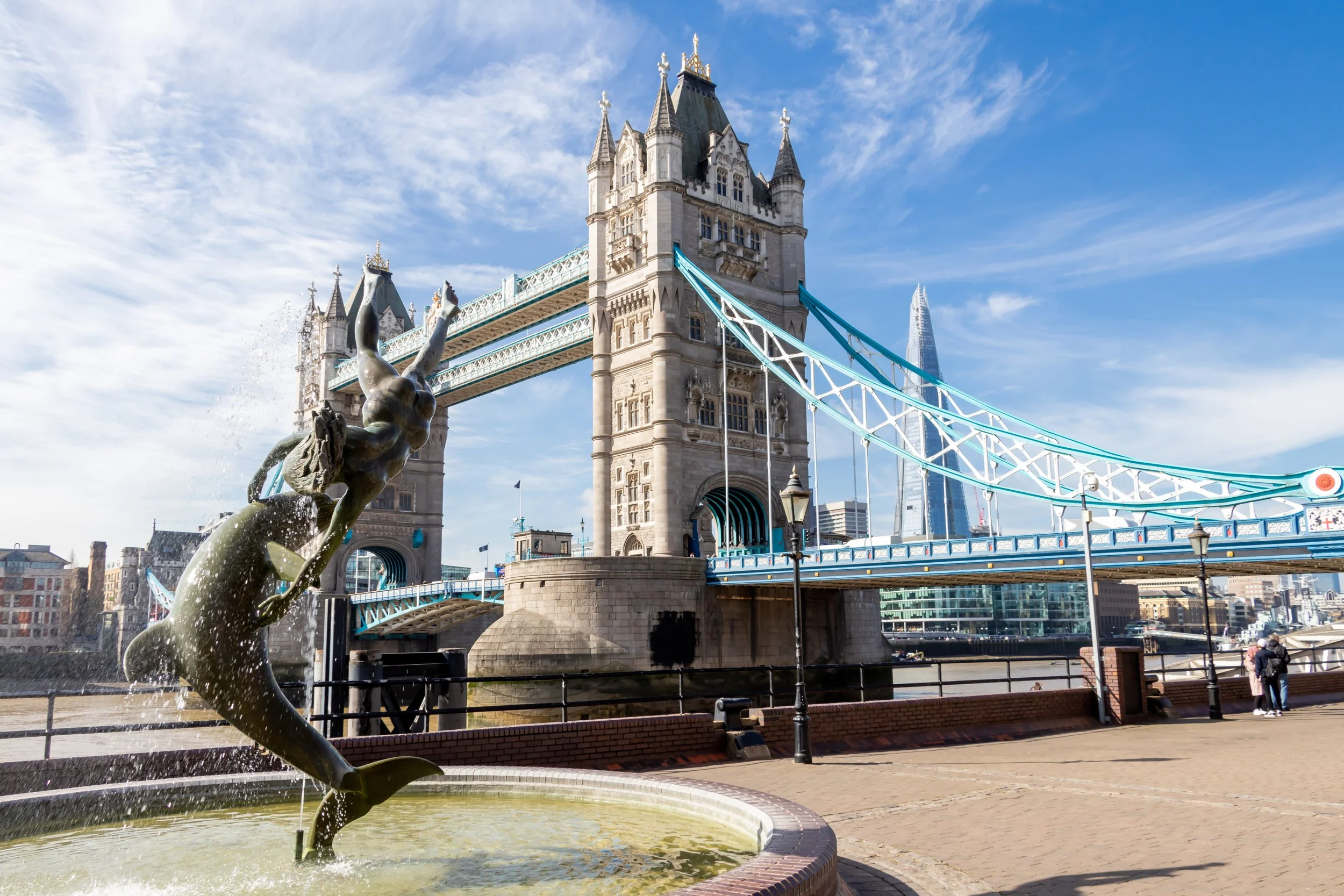London's Tower Bridge with a dolphin fountain in the foreground and the Shard skyscraper in the background on a clear day.