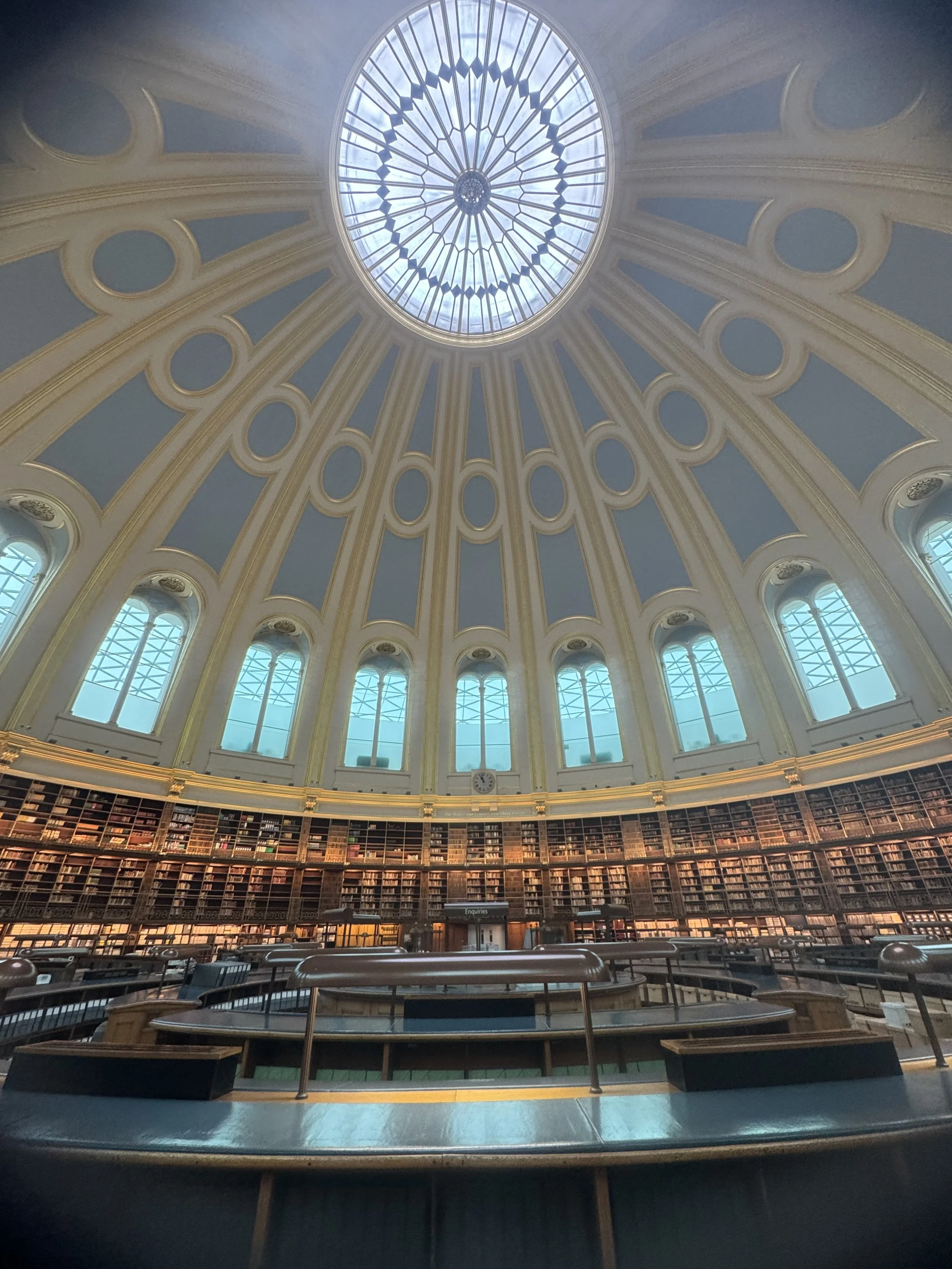 Interior view of a grand library with a domed glass ceiling and library shelves curving around the room.