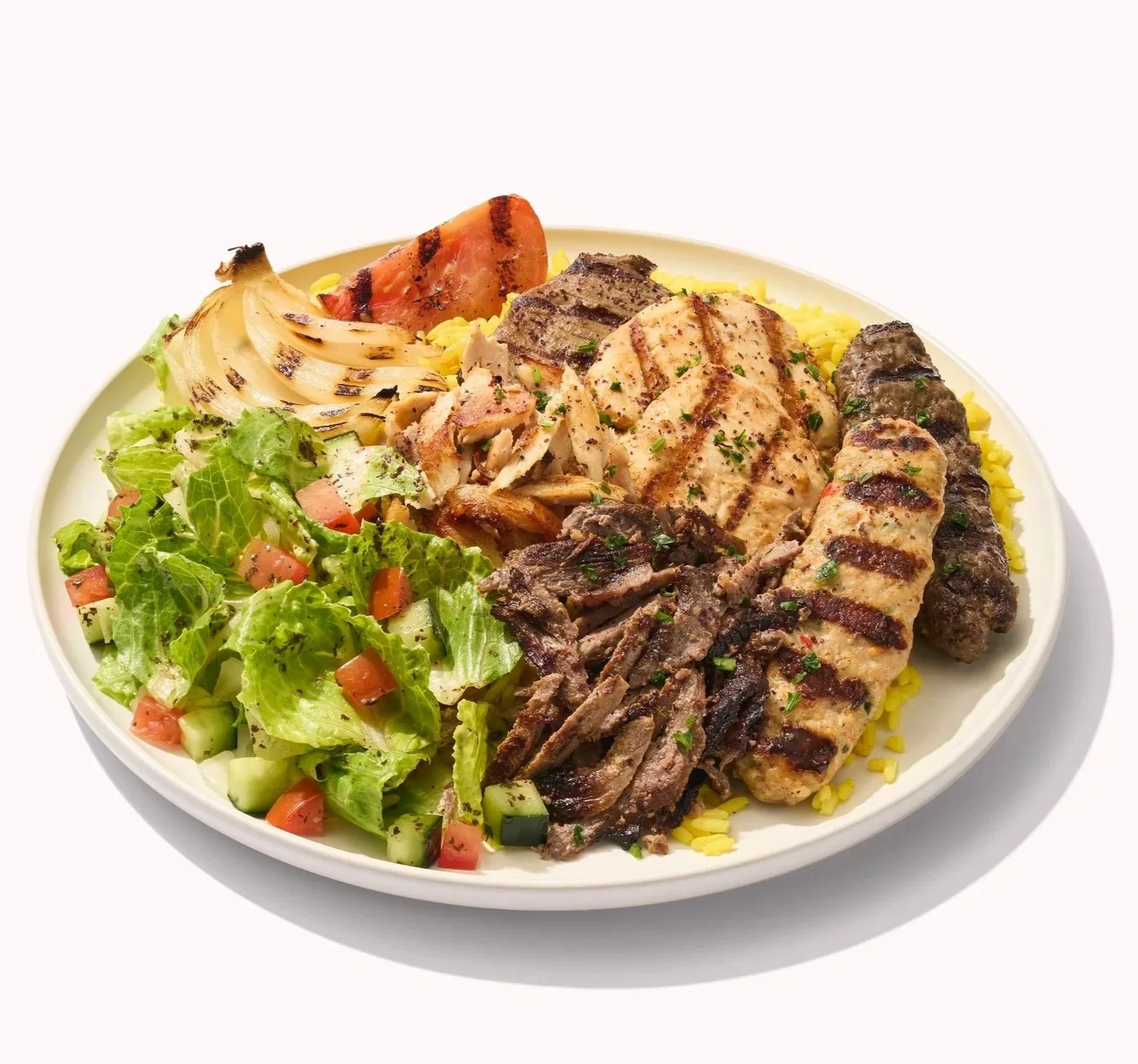 White plate filled with mediterranean food including chicken and beef with salad, rice and grilled vegetables on a white background.