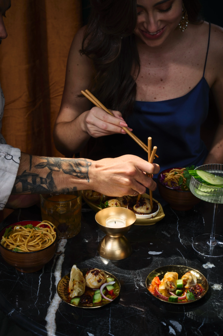 Man and woman sitting at a table on a date in a restaurant. Eating asian food with chopsticks with candle light.