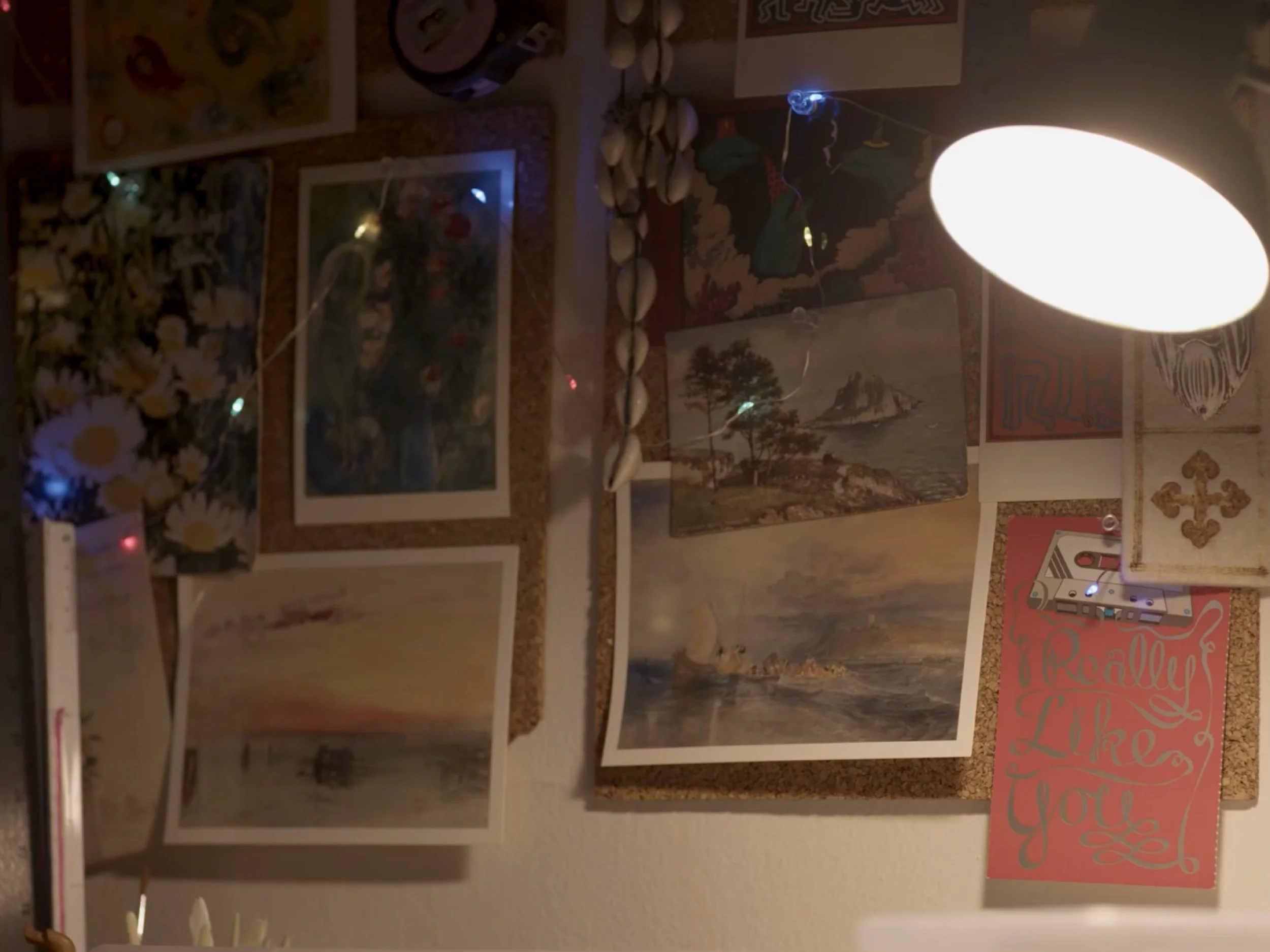 Wall decorated with various framed pictures, posters, and artwork, including a tapestry, a 'You Are Loved' sign, and other decorative pieces.