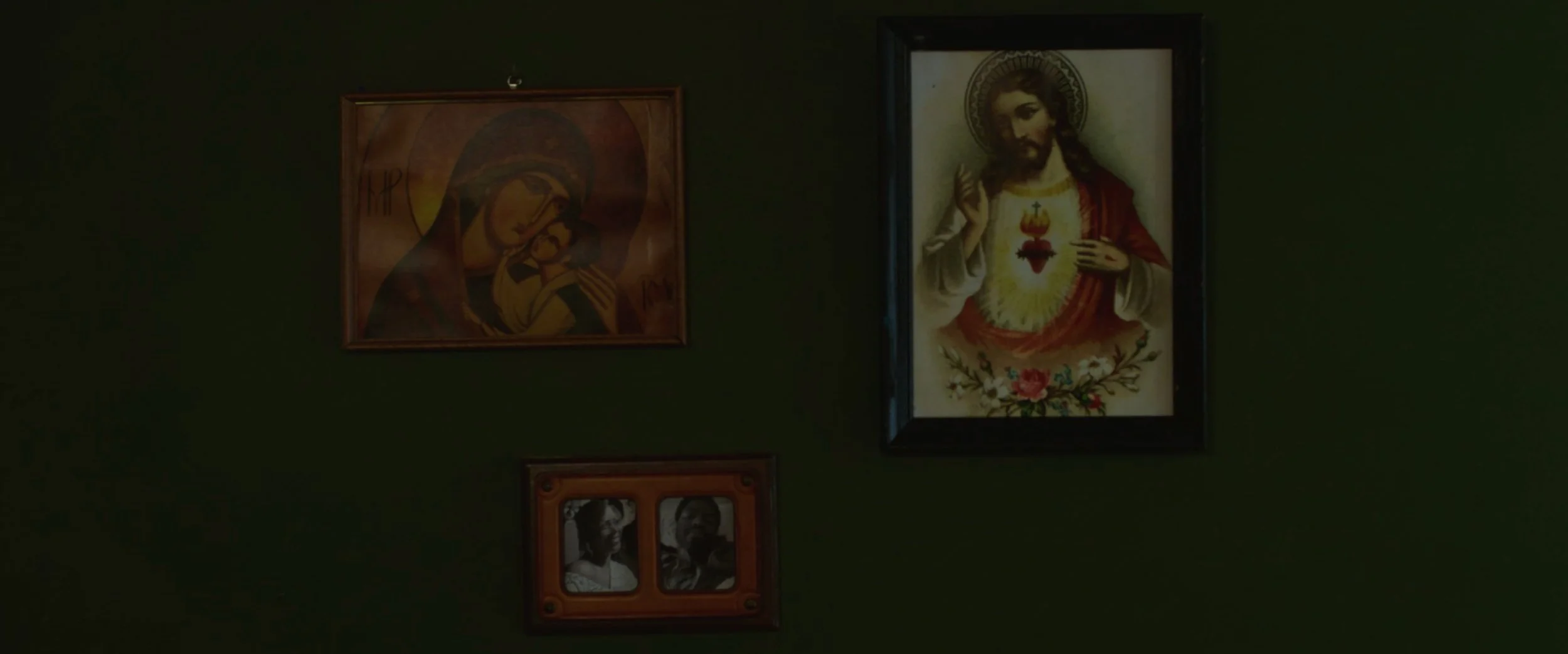Religious artwork on a dark green wall featuring images of Jesus and saints.