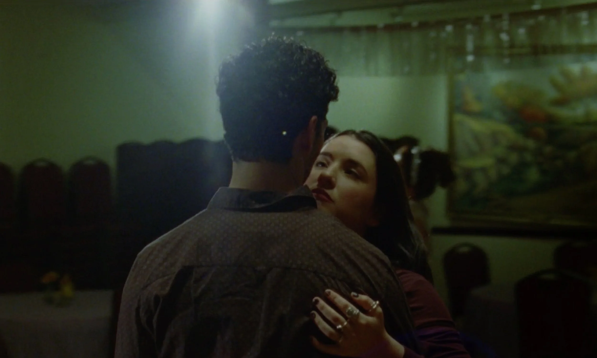 A man and a woman dancing closely together in a dimly lit room, with the woman looking up at the man and smiling.