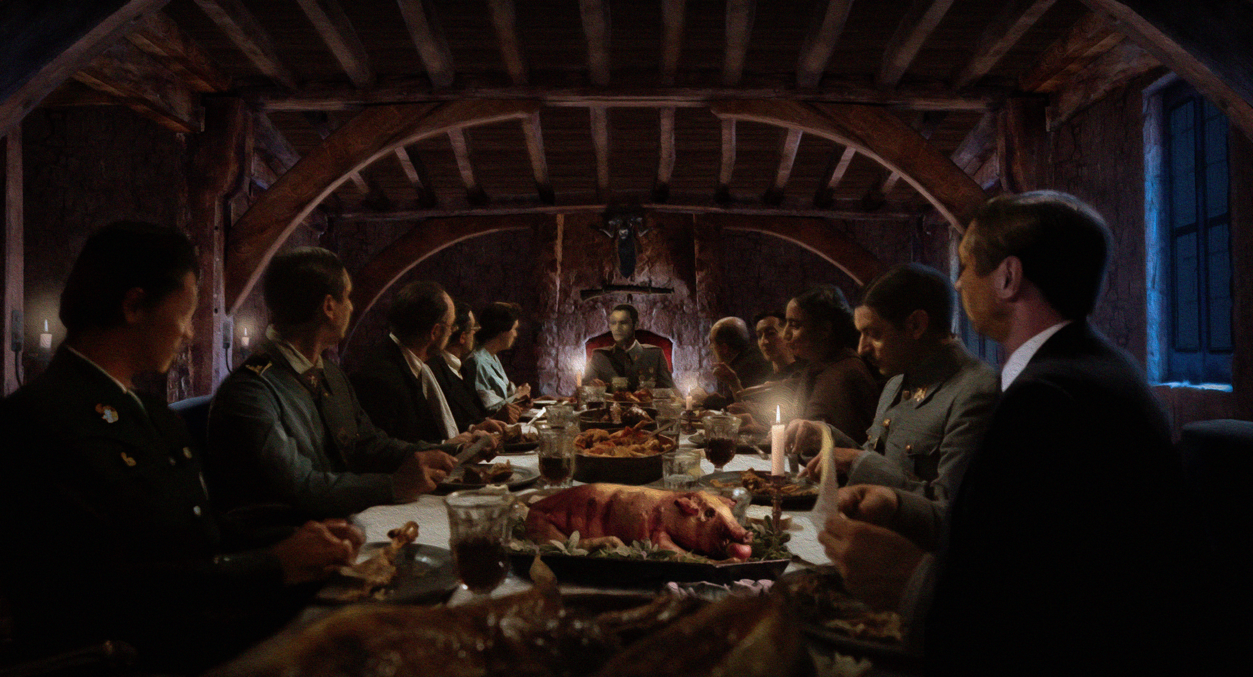 A group of people in military uniforms sitting at a banquet table with food, wine, and a candle, in a rustic stone and wood room.