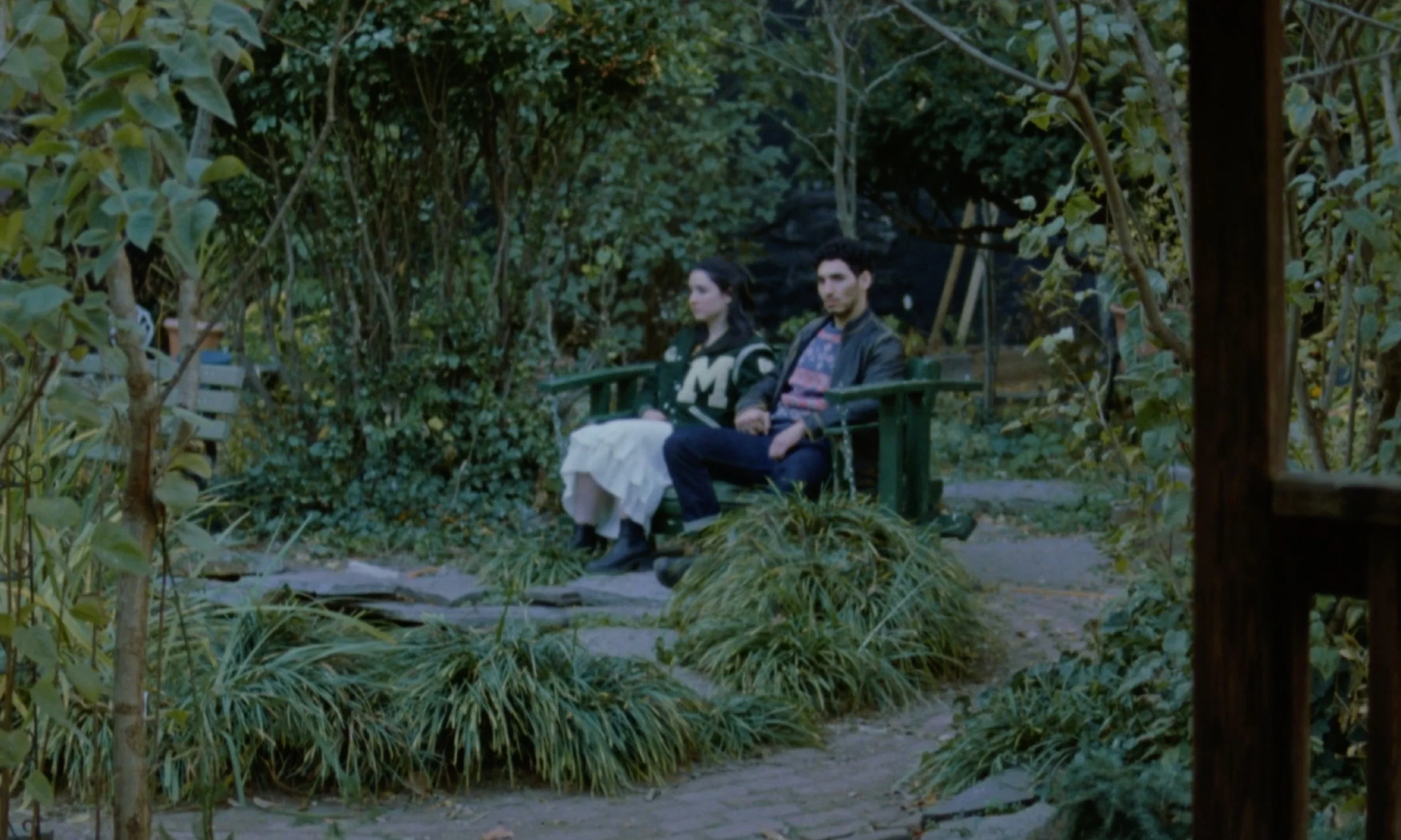 A man and woman sitting on a park bench surrounded by greenery and trees.