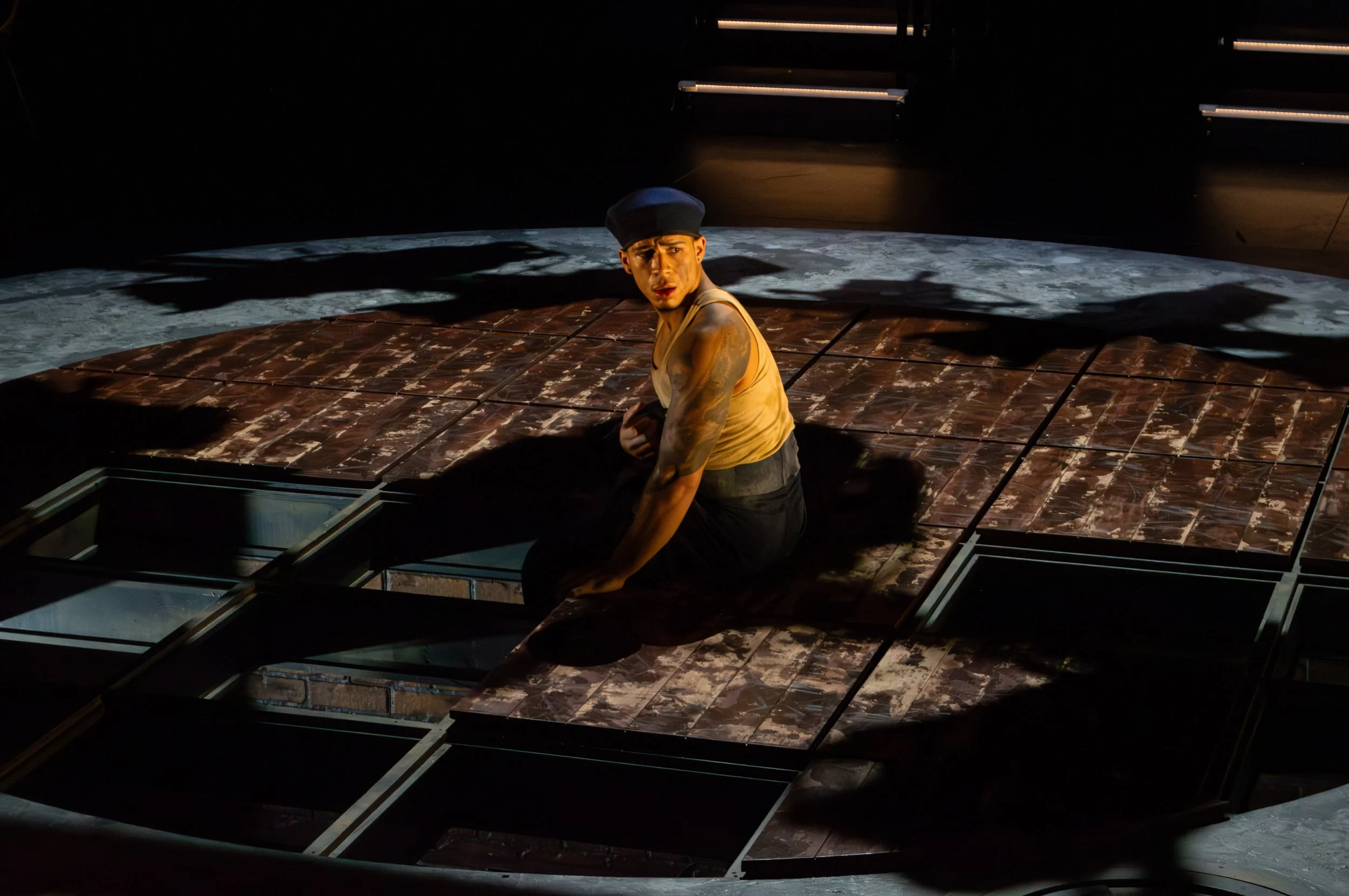 Performer with tattoos and a black cap on a stage with a moon backdrop.