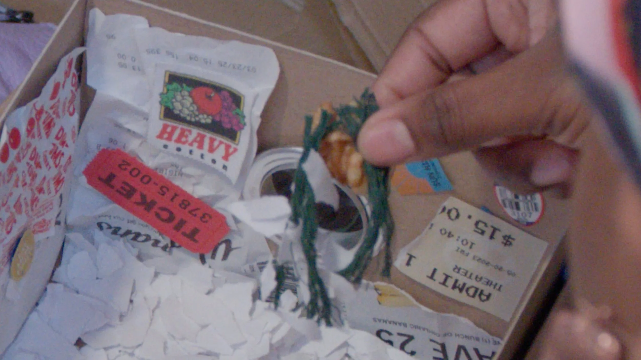 Close-up of a person's hand holding a small item, beside crumpled receipts and a box with various papers and a few stickers, including a partially visible billboard receipt.