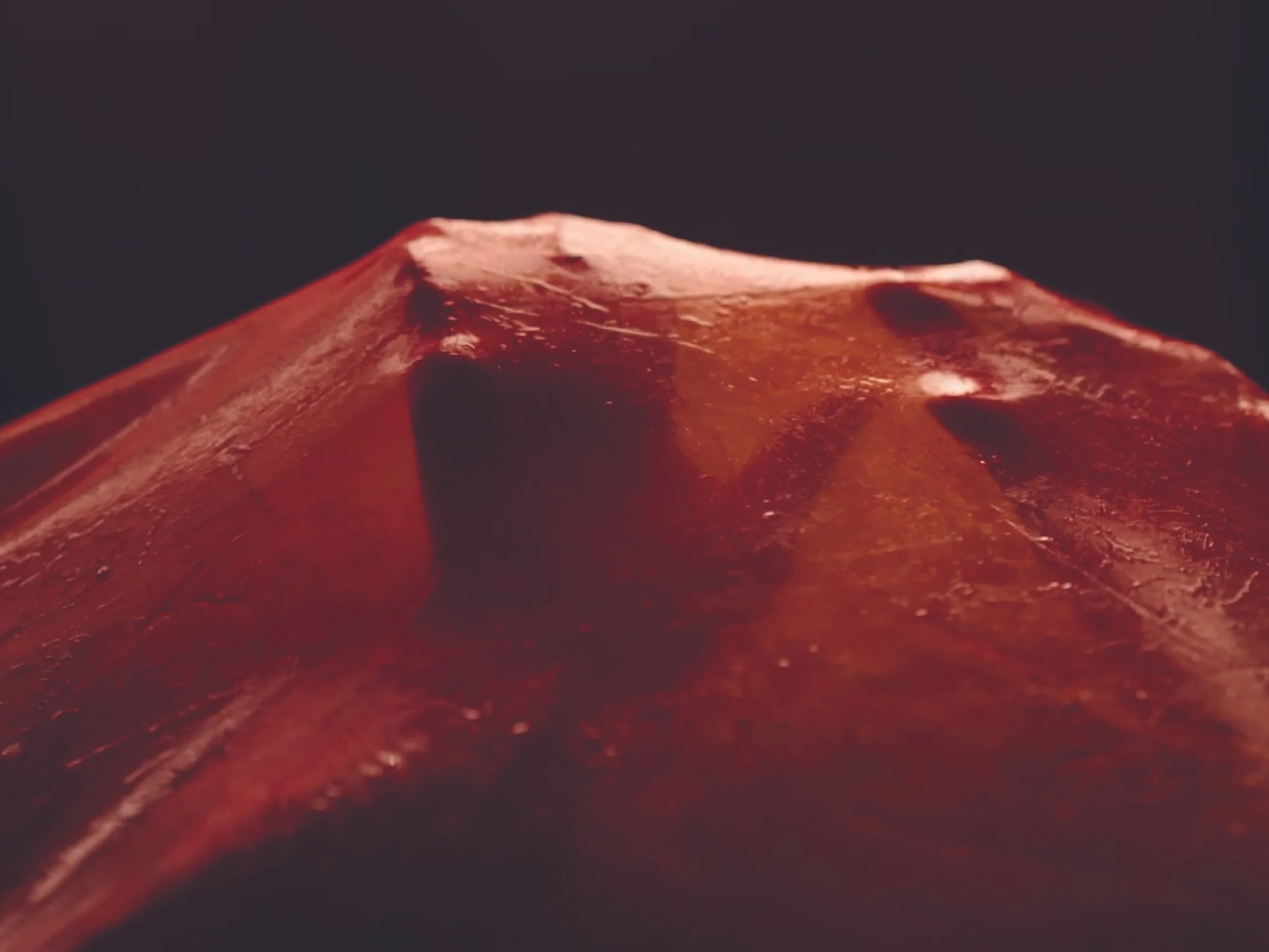 Close-up of a red gemstone with a smooth, polished surface against a dark background.