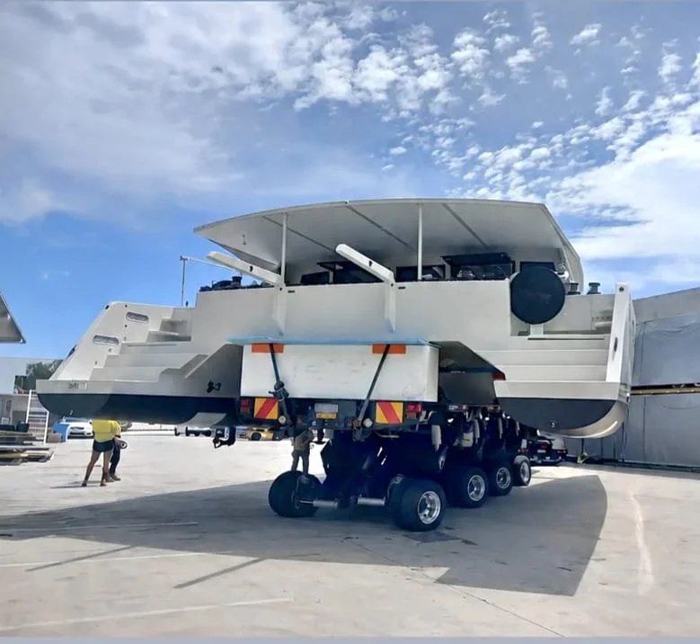 A large, complex piece of industrial or transportation equipment mounted on a trailer with multiple wheels, parked outdoors under a partly cloudy sky.