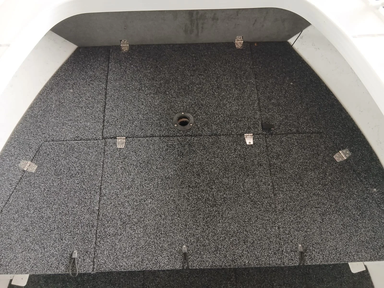 The image shows the inside of a cabinet with black carpeted flooring and metal hinges and a central round opening for a computer or electronic device.