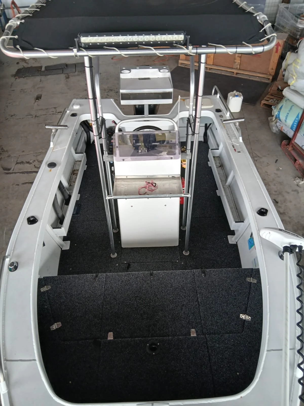 An empty boat with a steering console, LED light bar on the roof, and covered floor area, situated in what appears to be a storage or workshop space.
