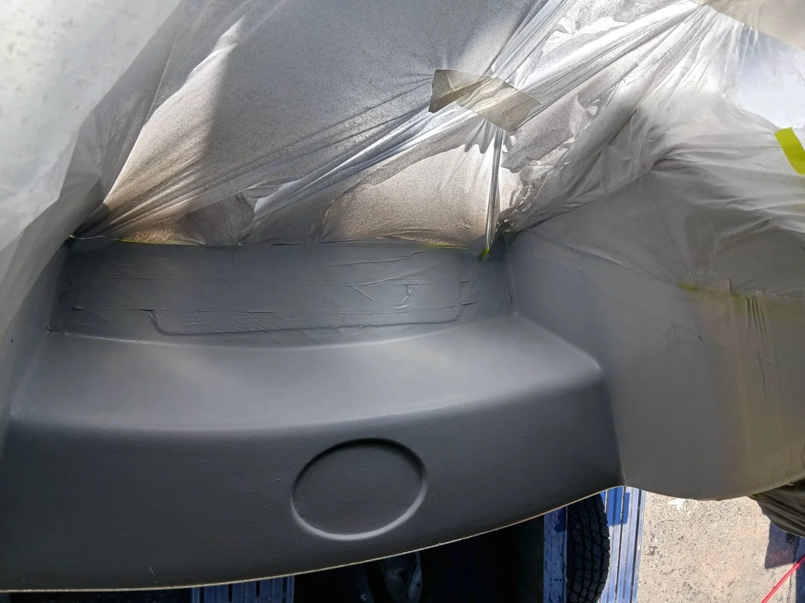 The image shows the front bumper of a vehicle with some tape and plastic covering around it, likely during a repair or painting process.