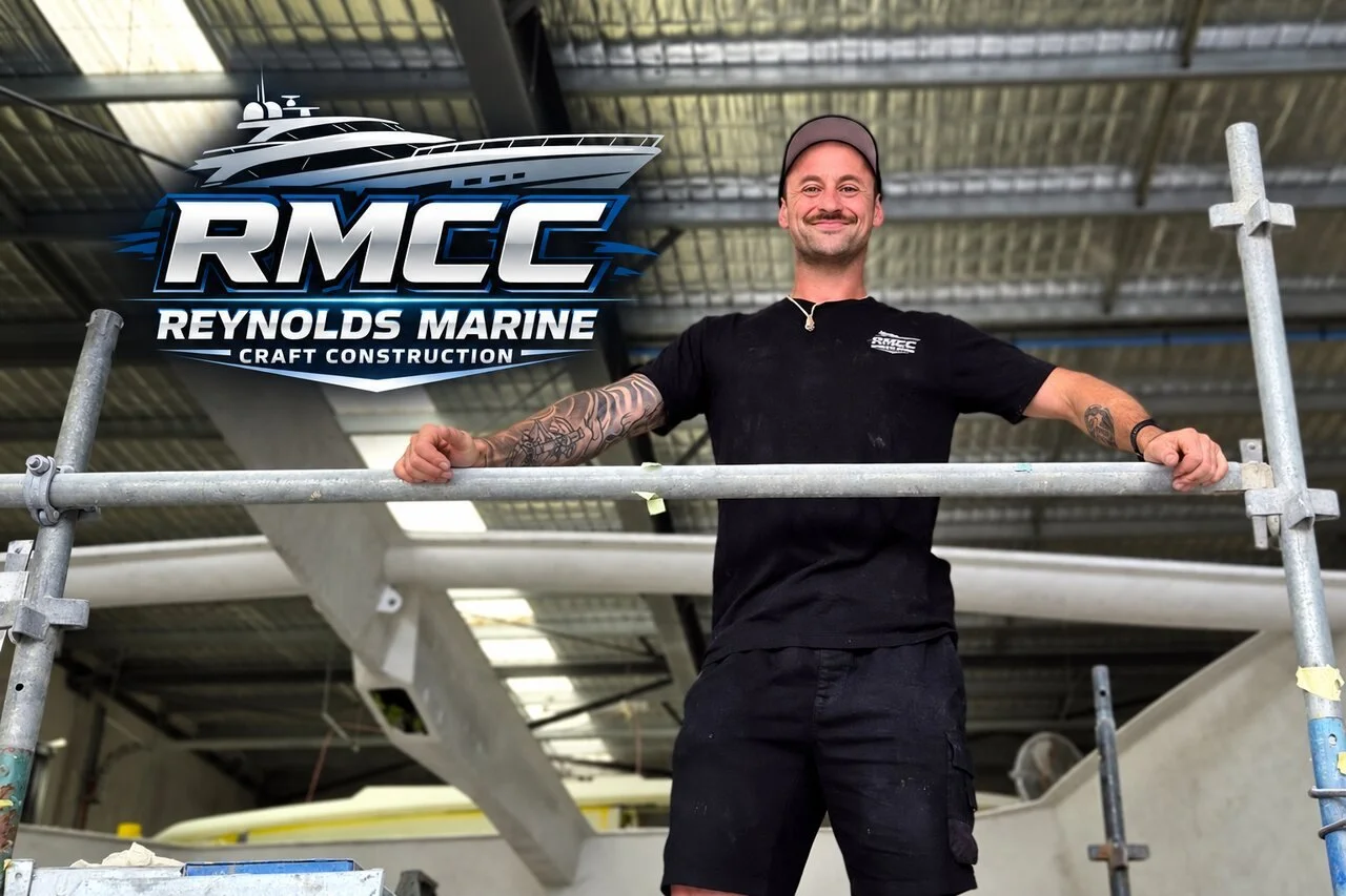 Joel Carnes, RMCC shipwright, in the Coolum workshop with the Reynolds Marine Craft Construction logo.