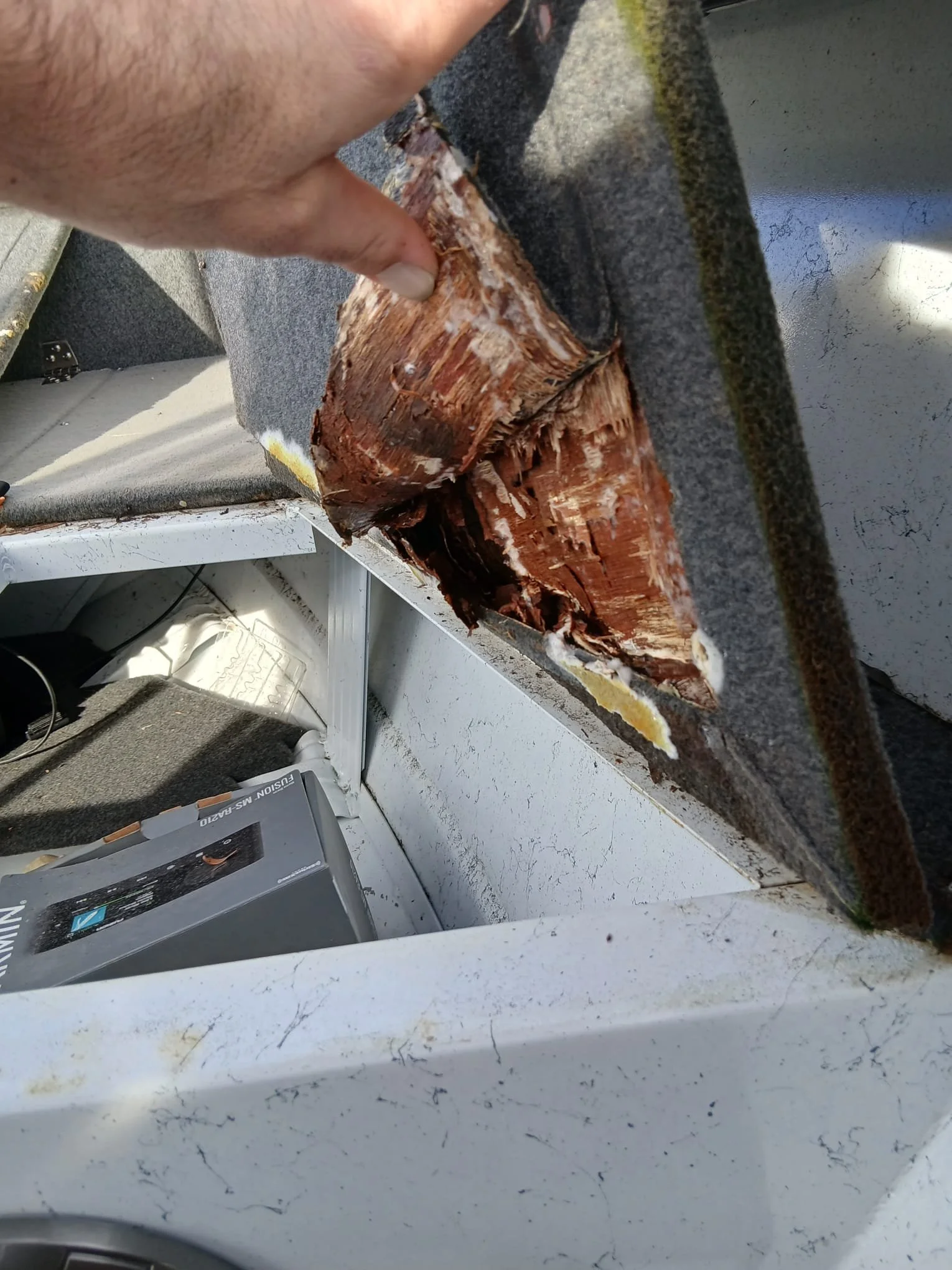 A person testing a piece of wood with a metal tool, possibly a chisel or similar, on a gray work surface. The work area shows signs of use, with marks and wood debris.