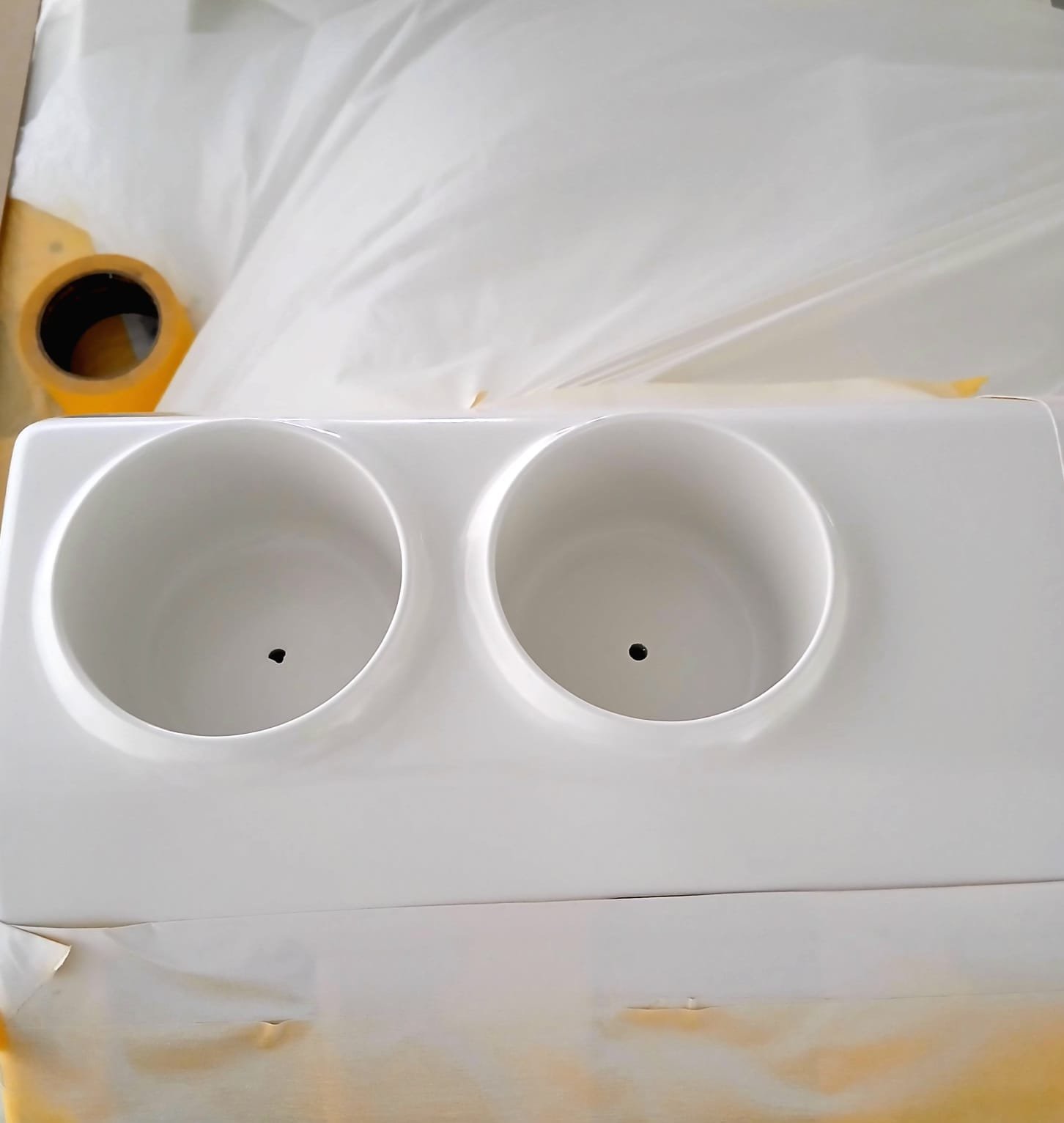 White plastic container with two circular compartments, each with a small hole at the bottom, on top of a white surface, with a roll of yellow tape in the background.