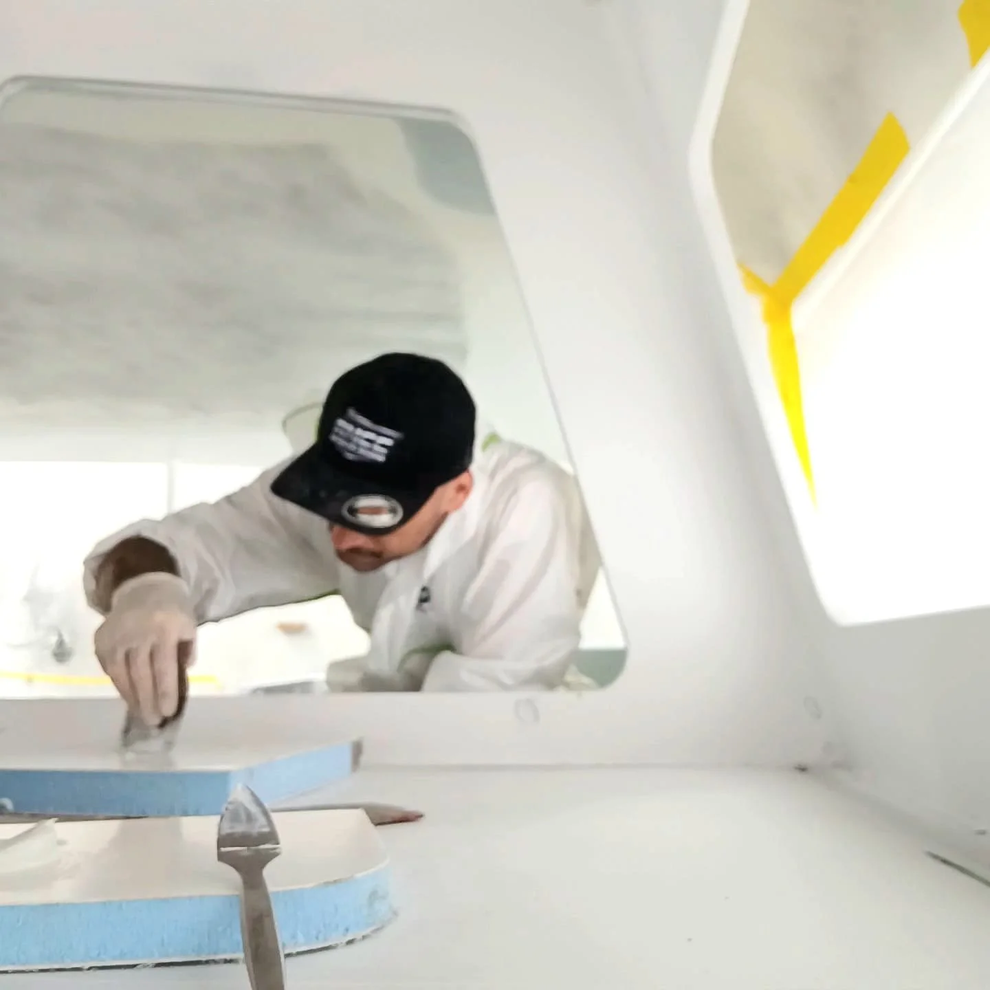 A person in white clothing and a black cap working on a craft project inside a white room with yellow accents.