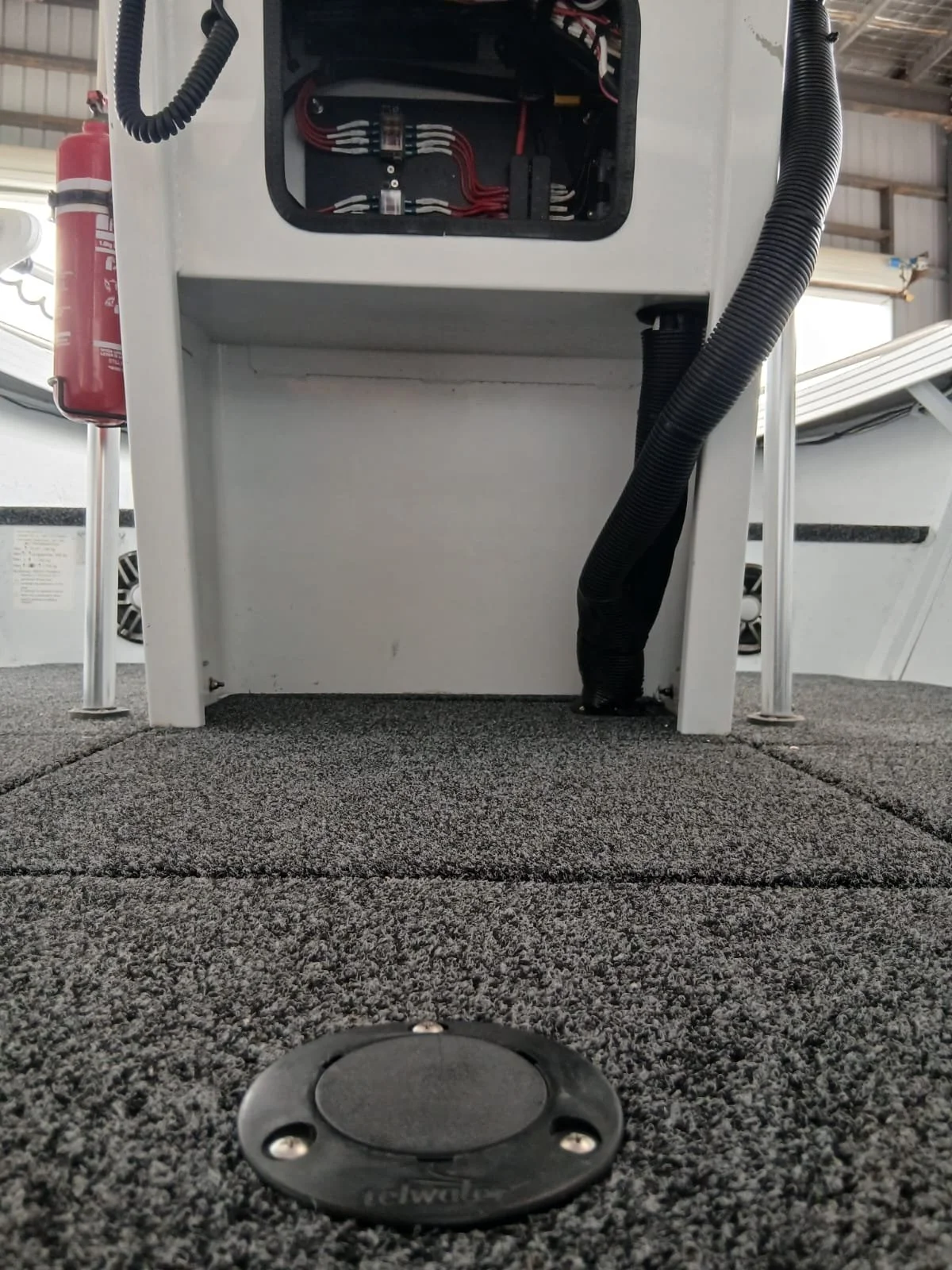 View from ground level of a desk with an open electrical box and black flexible conduit, in a warehouse or industrial setting.