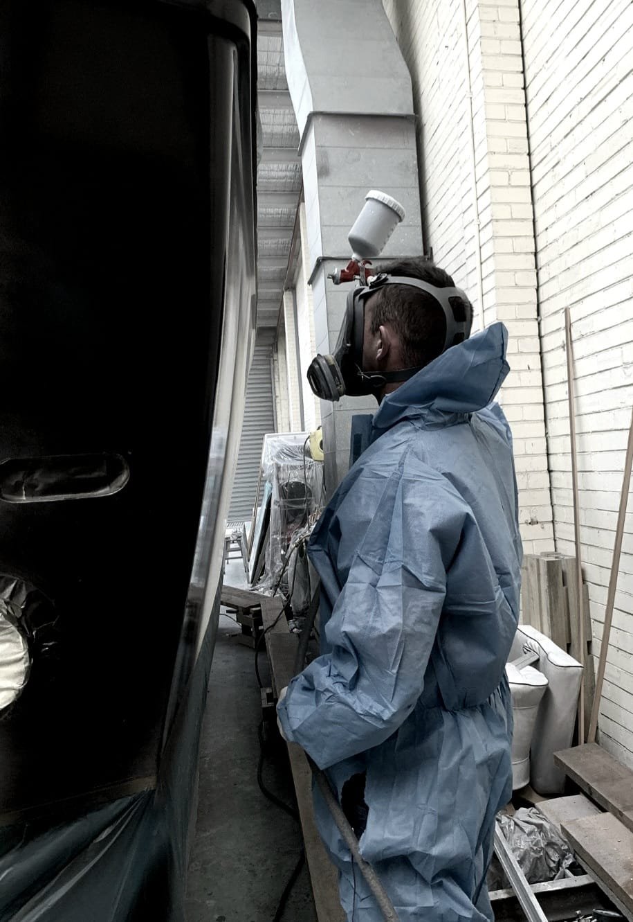 A person wearing a protective suit, mask, and face shield working with a paint sprayer.