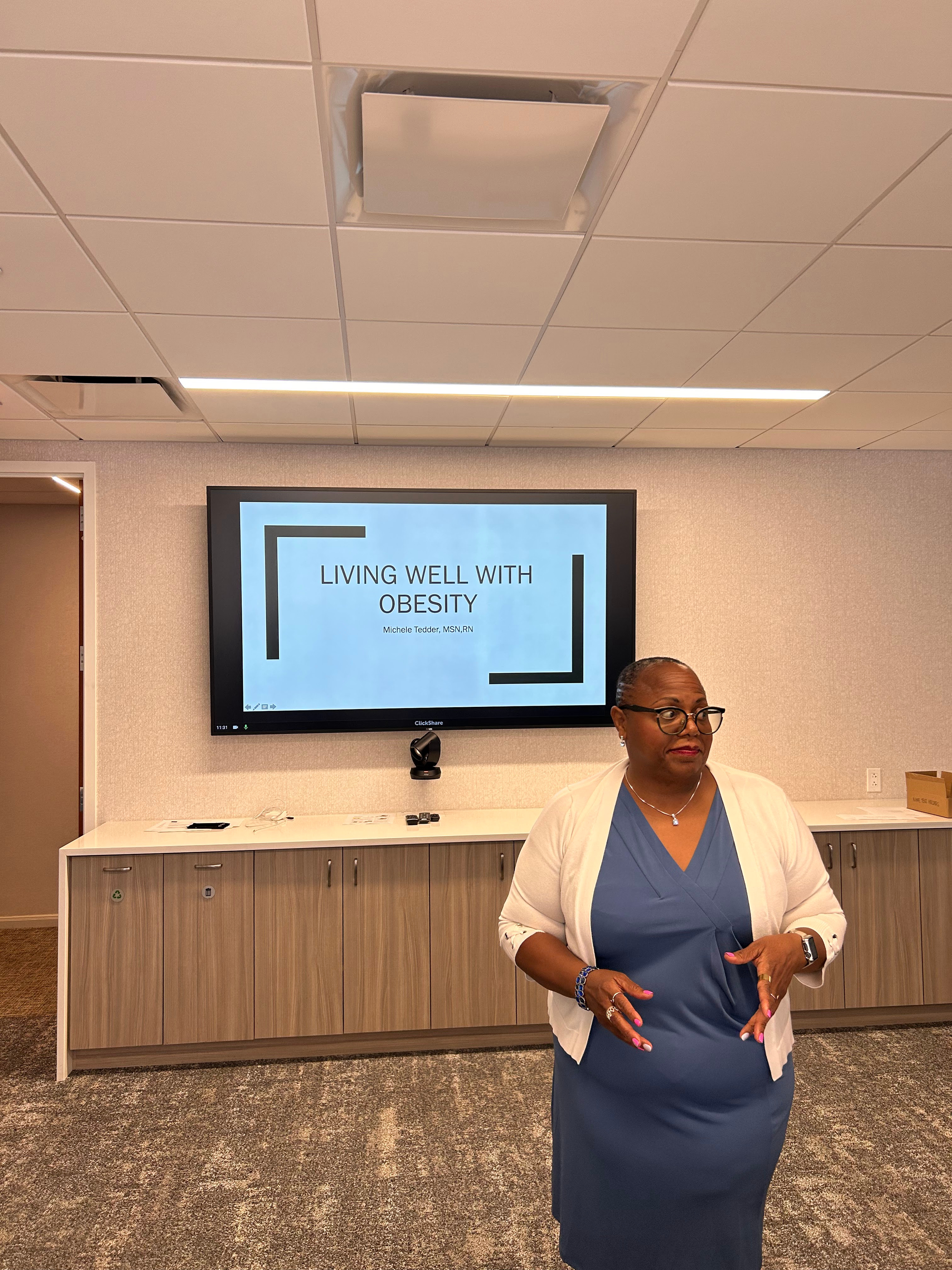 A woman in a blue dress and white blazer standing in front of a presentation screen in a conference room.