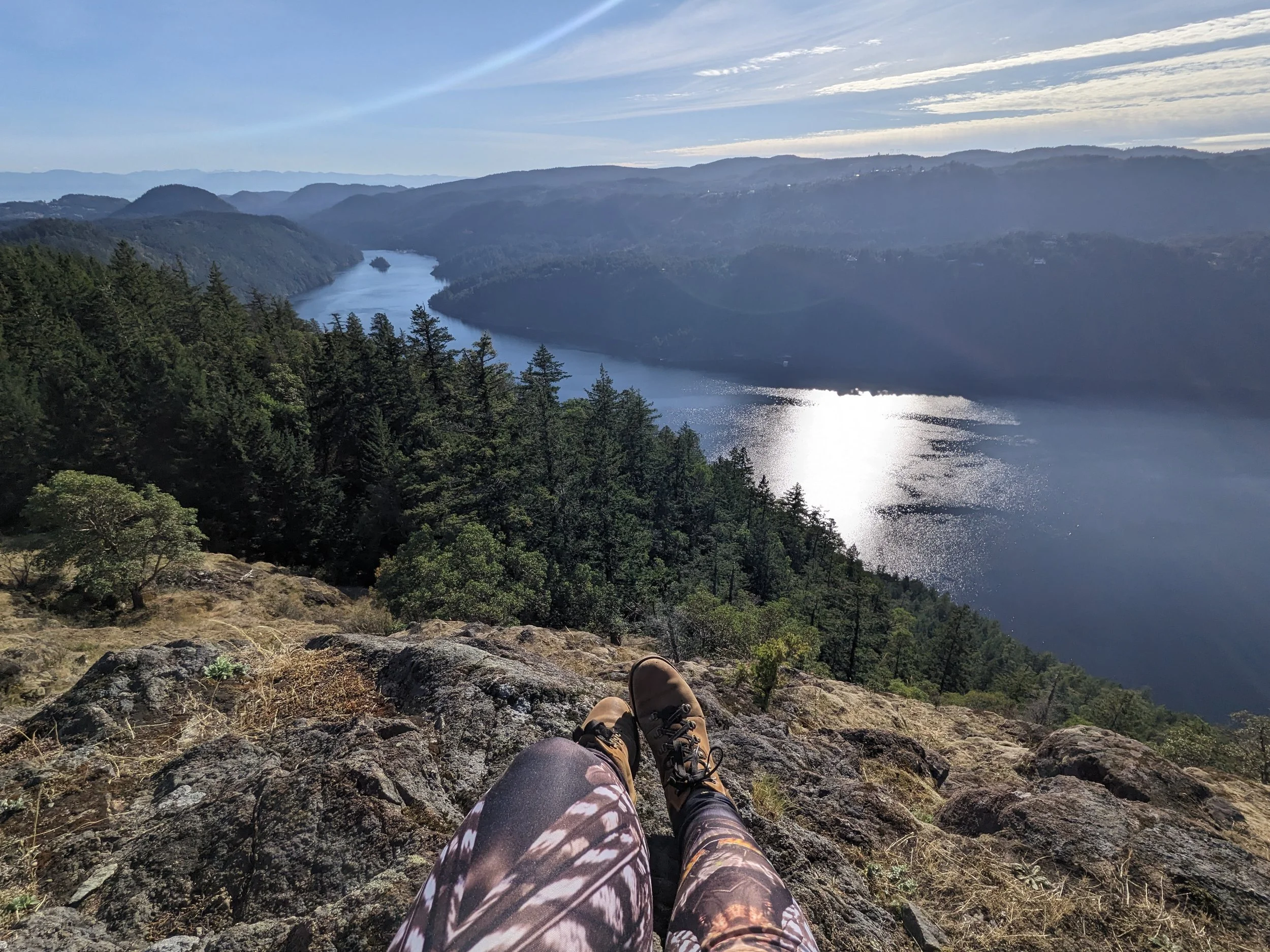 a Persons feet resting on a rocky outcrop overlooking a river and miles of open forest.