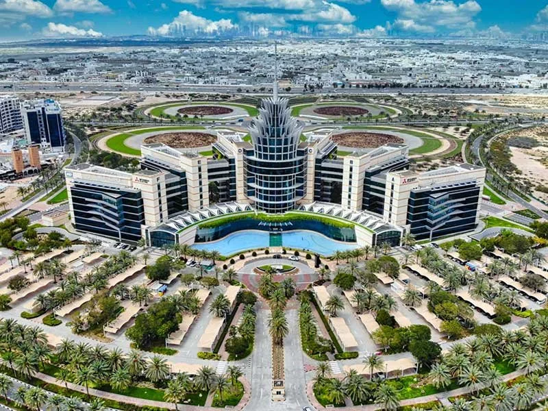 Aerial view of the Dubai Silicon Oasis headquarters with a fountain and pool in front, surrounded by palm trees and gardens, with a circular driveway and parking lots.