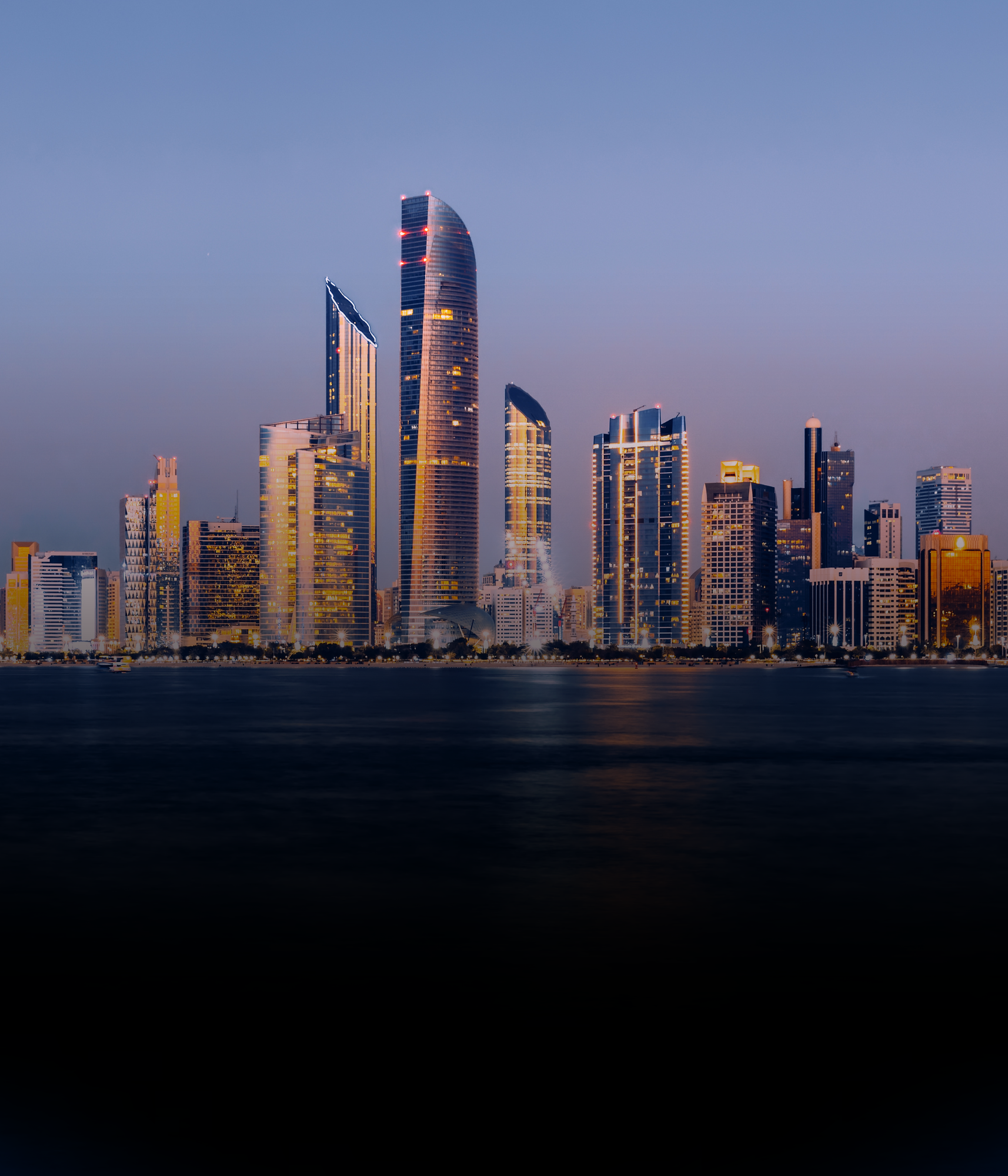 Abu Dhabi city skyline with tall, illuminated skyscrapers reflecting on a water body in the foreground.
