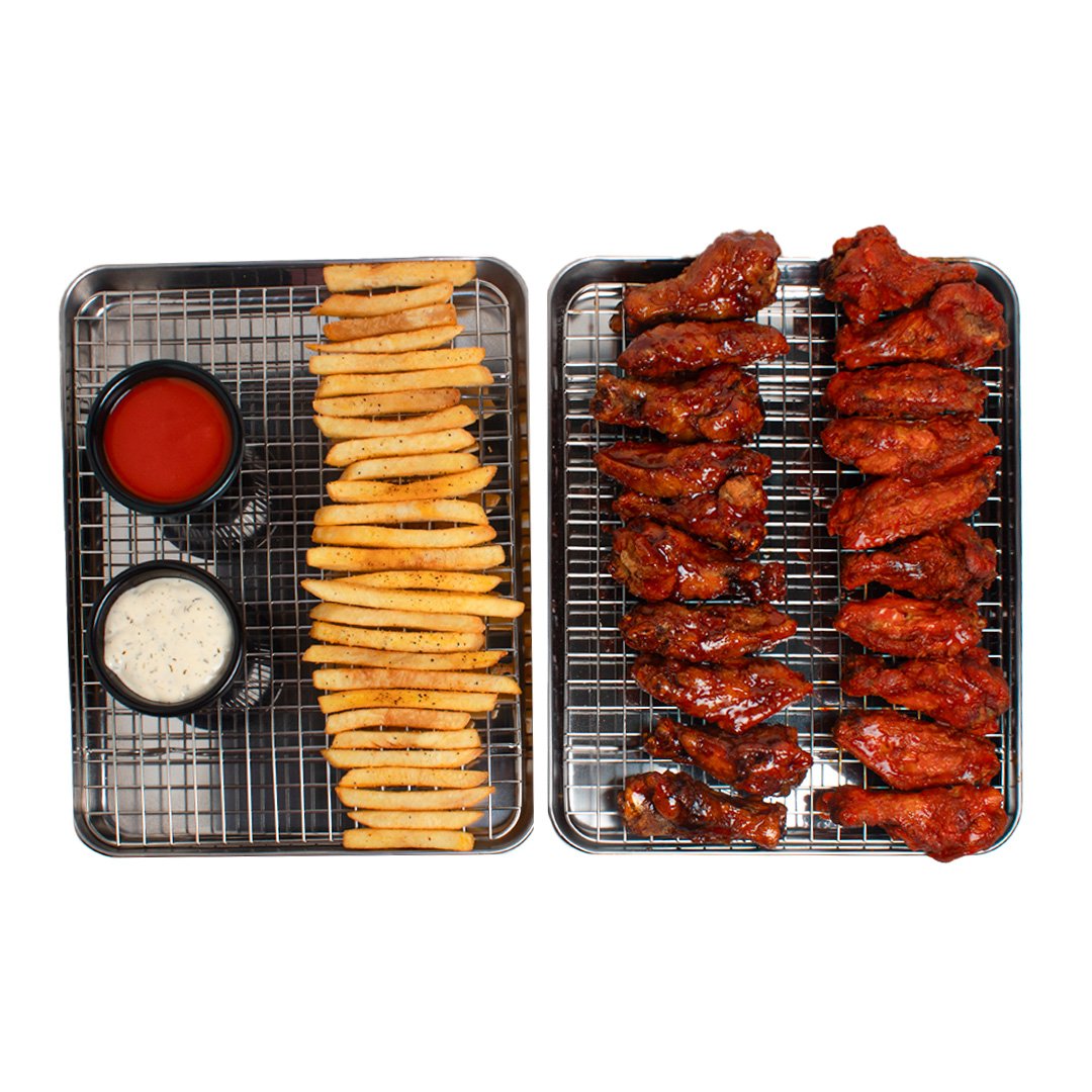 Two metal trays of food with French fries, chicken wings, and dipping sauces, set against a white background.