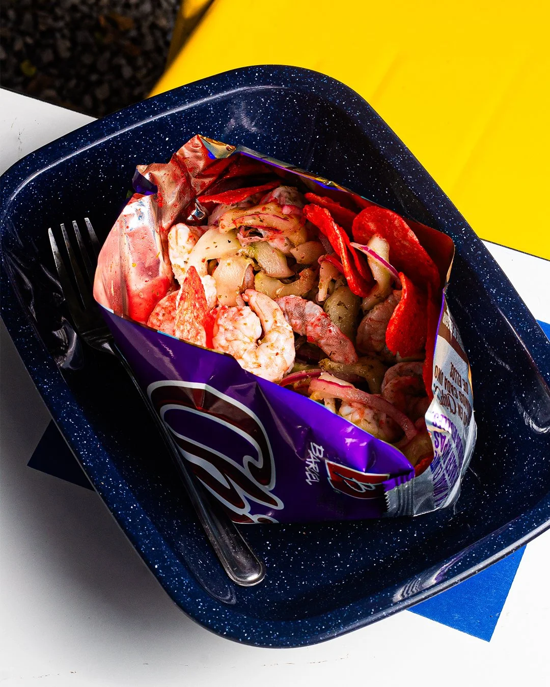 Seafood salad in a purple bag placed in a speckled blue bowl with a fork and a blue napkin.