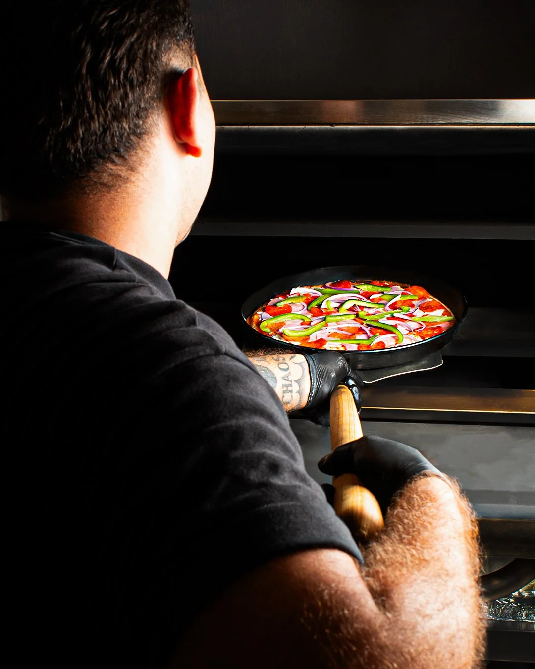 Pizzaiolo placing a pepperoni and vegetable pizza into an oven.