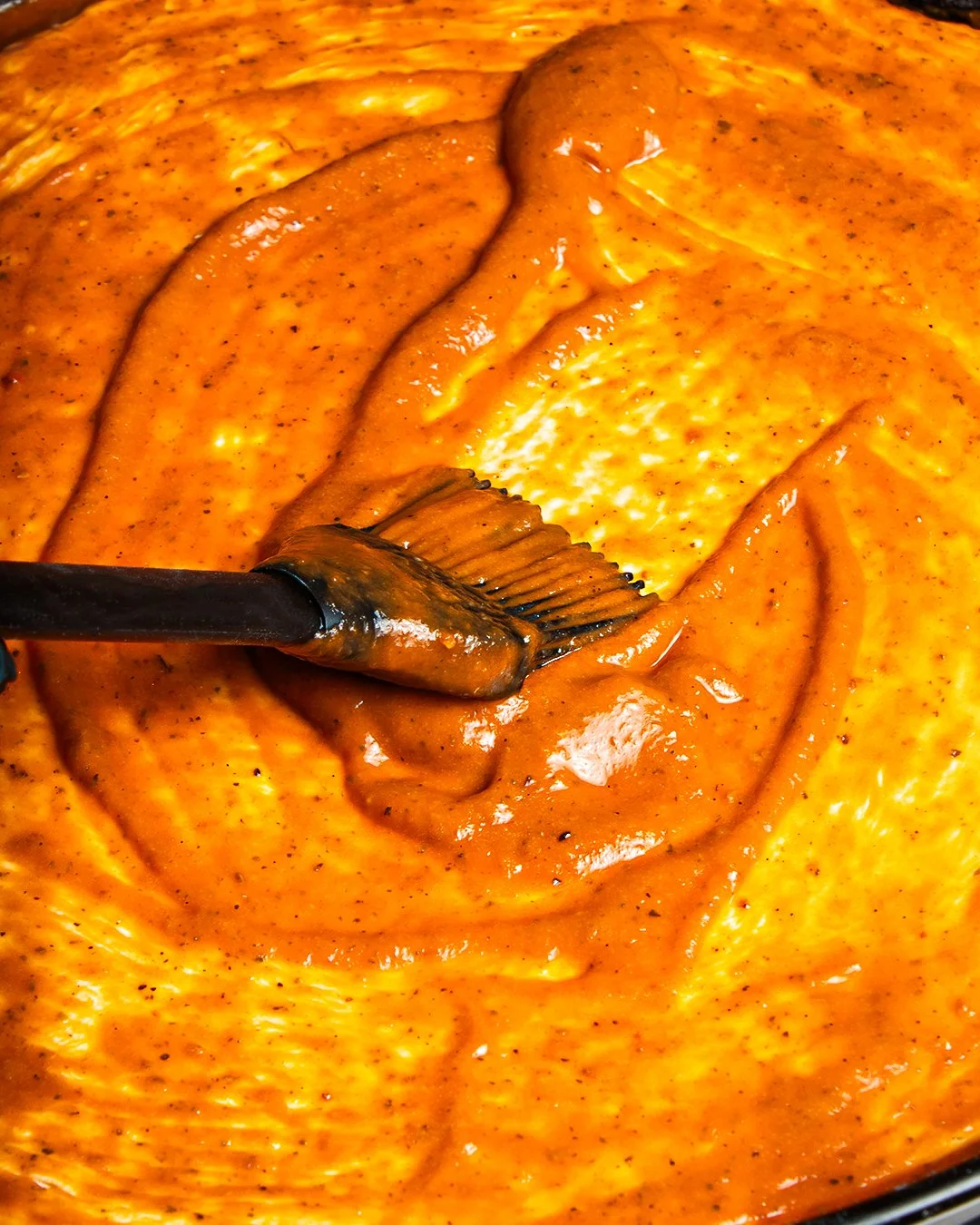 Close-up of thick orange sauce or curry being stirred with a spatula.