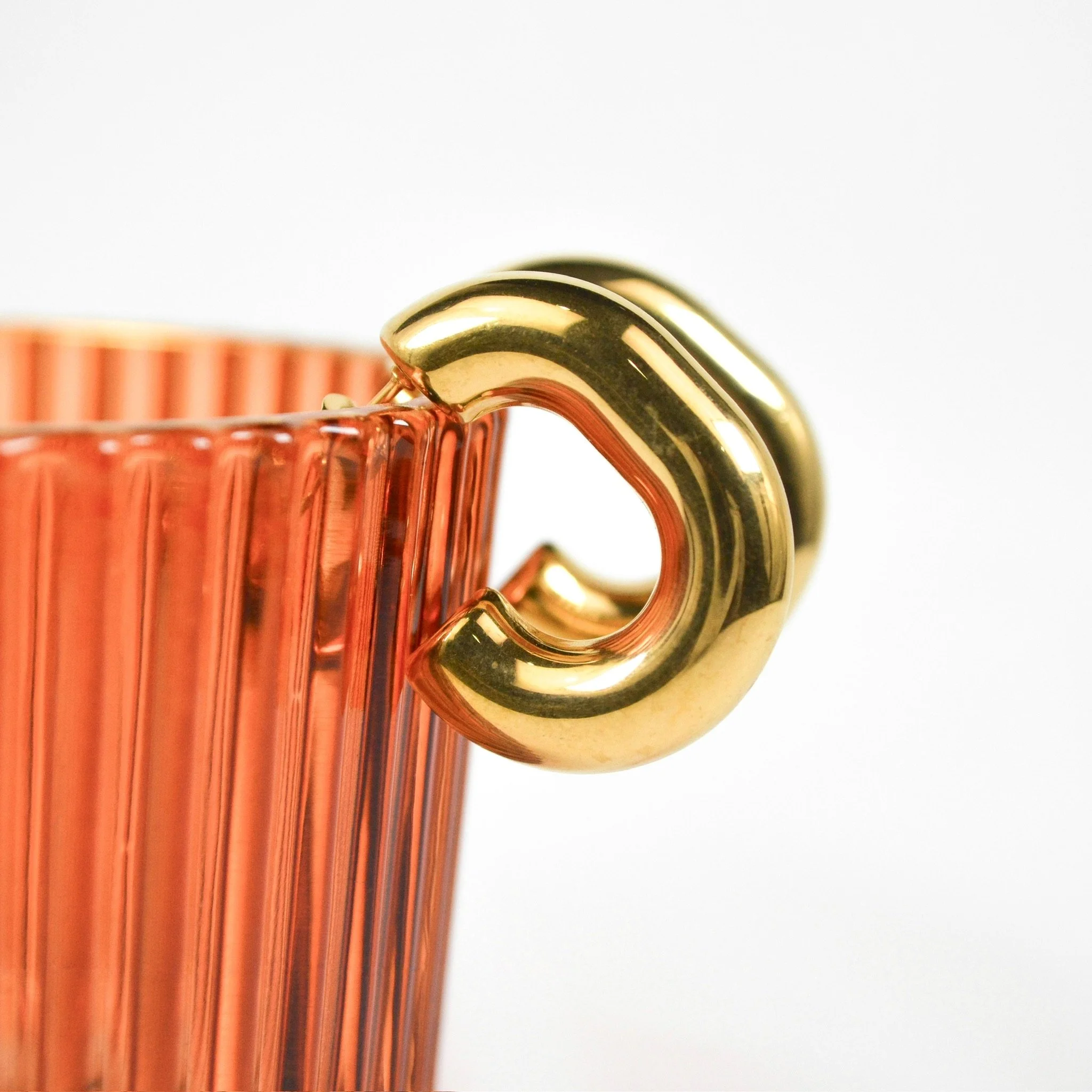 Close-up of a gold and black curved handle attached to a copper-colored ribbed glass container.