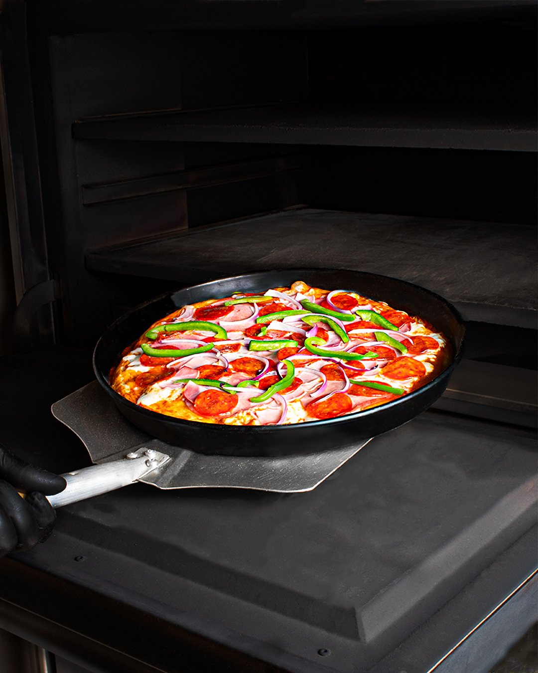 Homemade pizza with pepperoni, sliced onions, and green bell peppers baking in an oven.