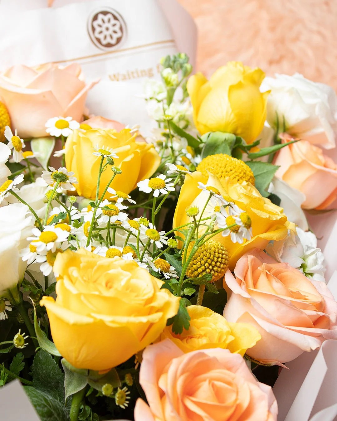 Close-up of a bouquet of yellow, white, and peach roses with small white daisies and green leaves.