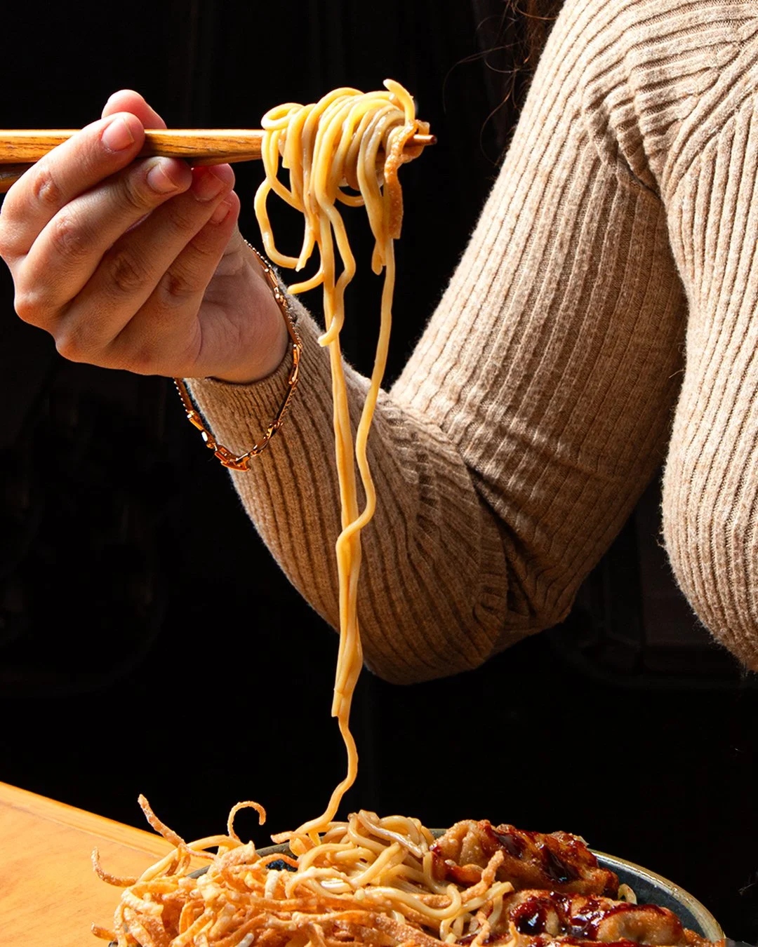 Person holding chopsticks with noodles above a plate of spaghetti with meatballs.