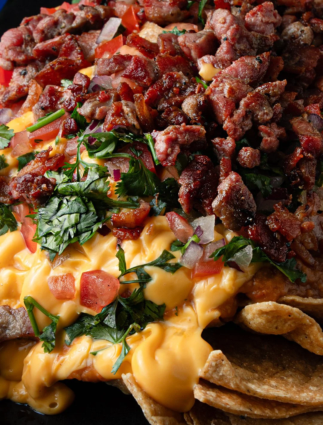 Close-up of nachos topped with seasoned ground beef, cheese sauce, chopped tomatoes, onions, jalapeños, and fresh cilantro.