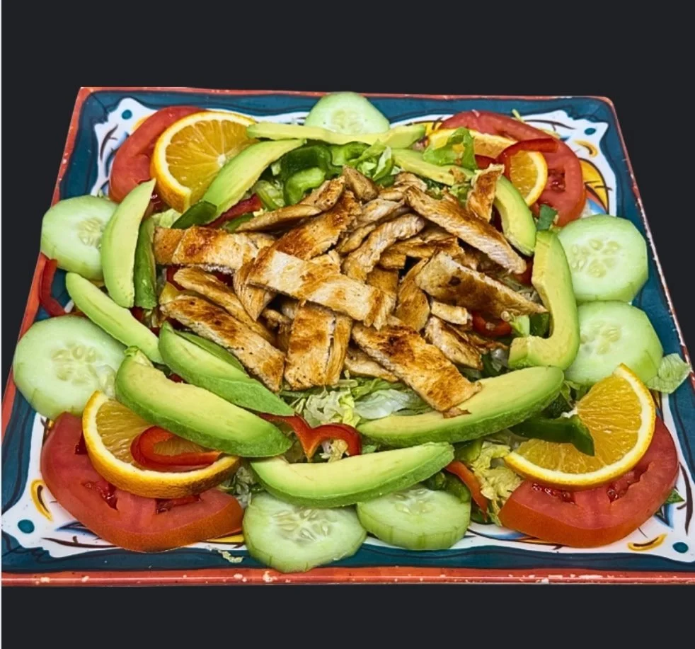 A colorful salad with grilled chicken, sliced cucumbers, tomatoes, red bell peppers, and orange wedges on a decorative square plate.