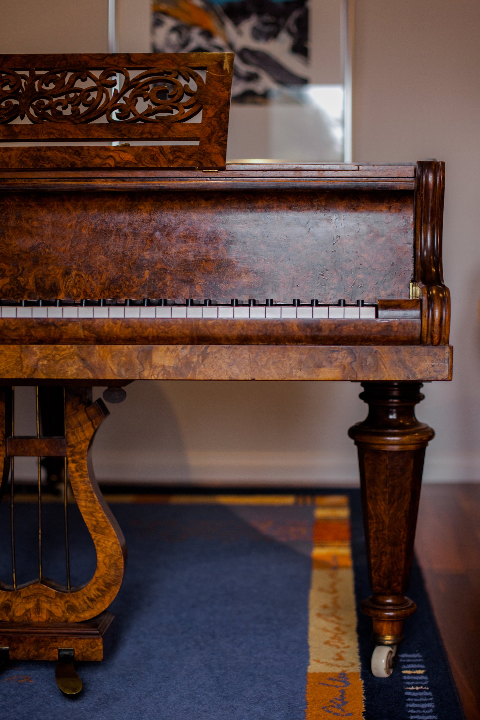 Close-up of a vintage wooden piano with intricate design on the music stand, set on a carpeted floor.